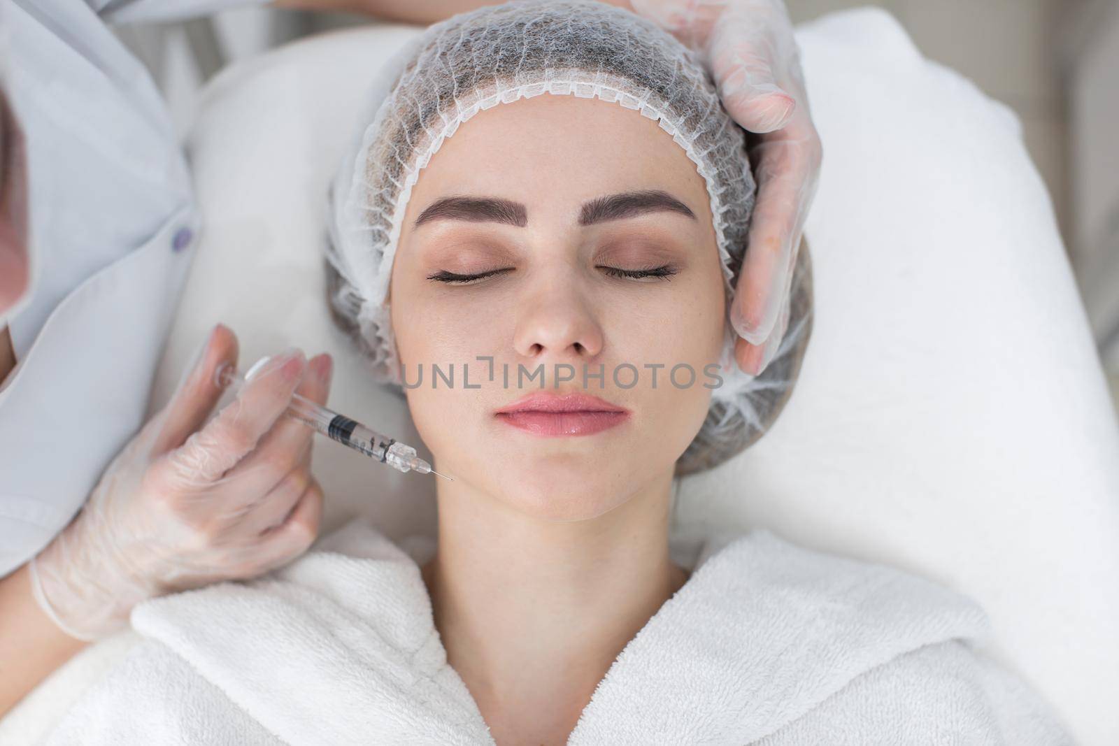 Hands of cosmetologist making injection in face, lips. Young woman gets beauty facial injections in salon. Face aging, rejuvenation and hydration procedures. Aesthetic cosmetology by StudioPeace