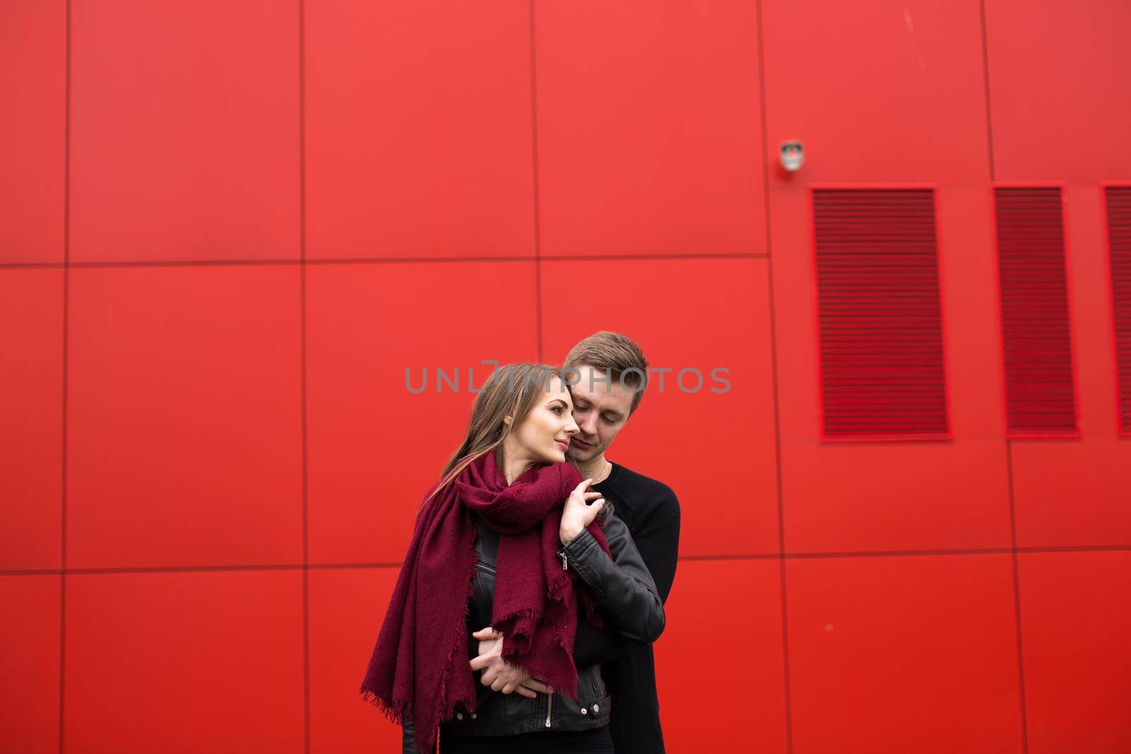 Young man and woman in passion, emotion, on the street with a backdrop of the red wall. Fashion. by StudioPeace