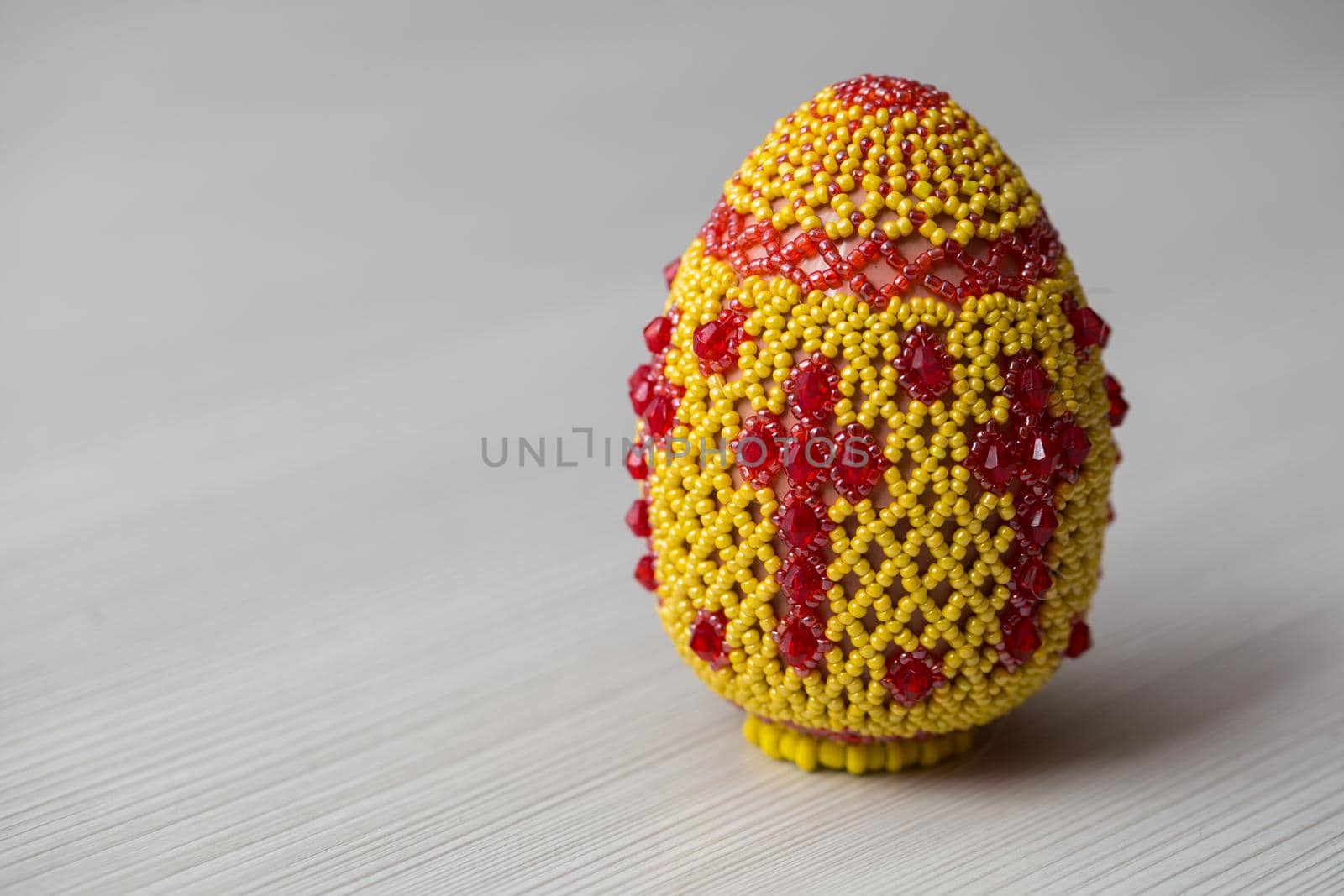 Egg decorated with small beads on a white table. by StudioPeace