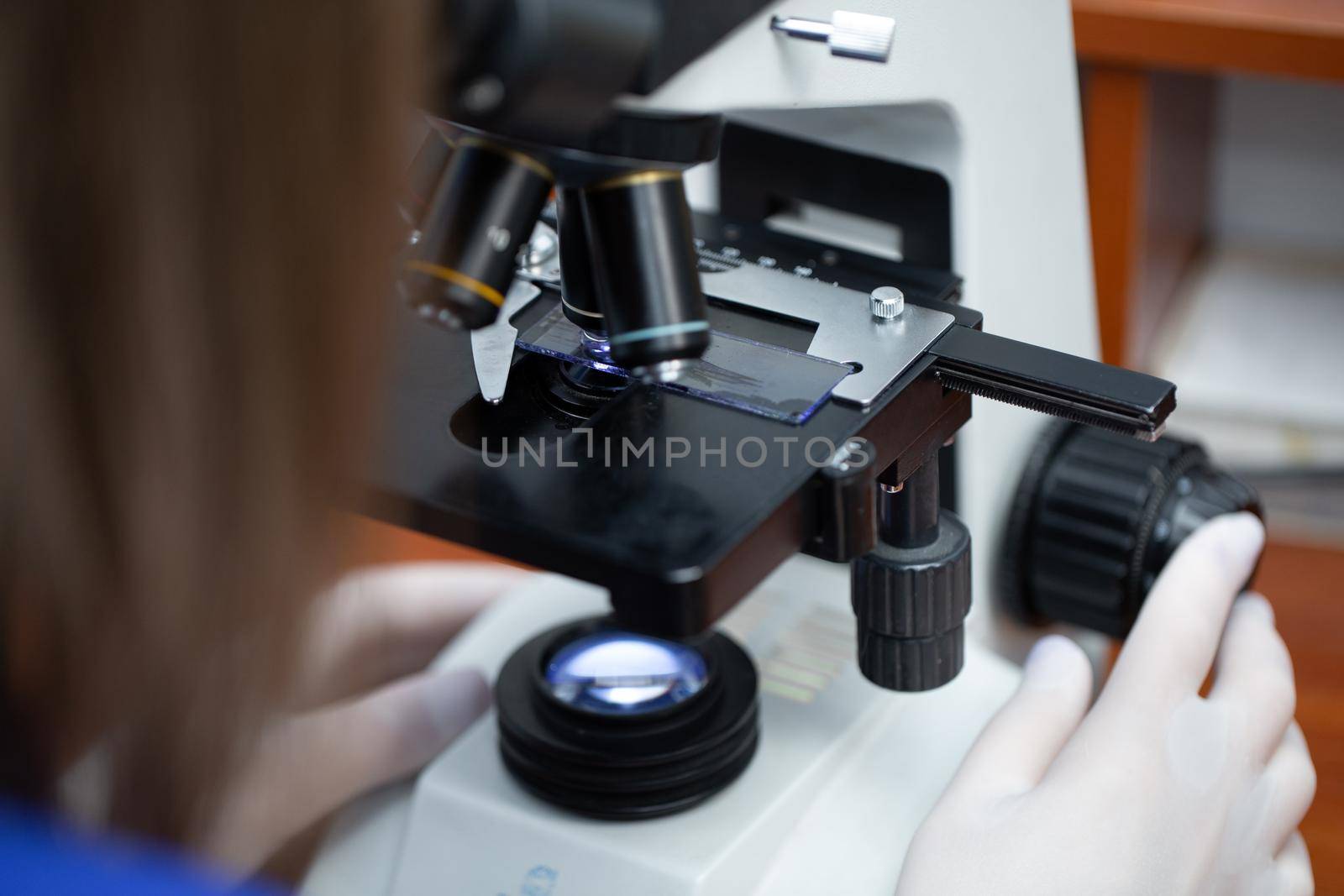 Young attractive veterinary worker in gloves using microscope for testing blood samples of animals. Vet doctor looking into microscope, close-up by StudioPeace