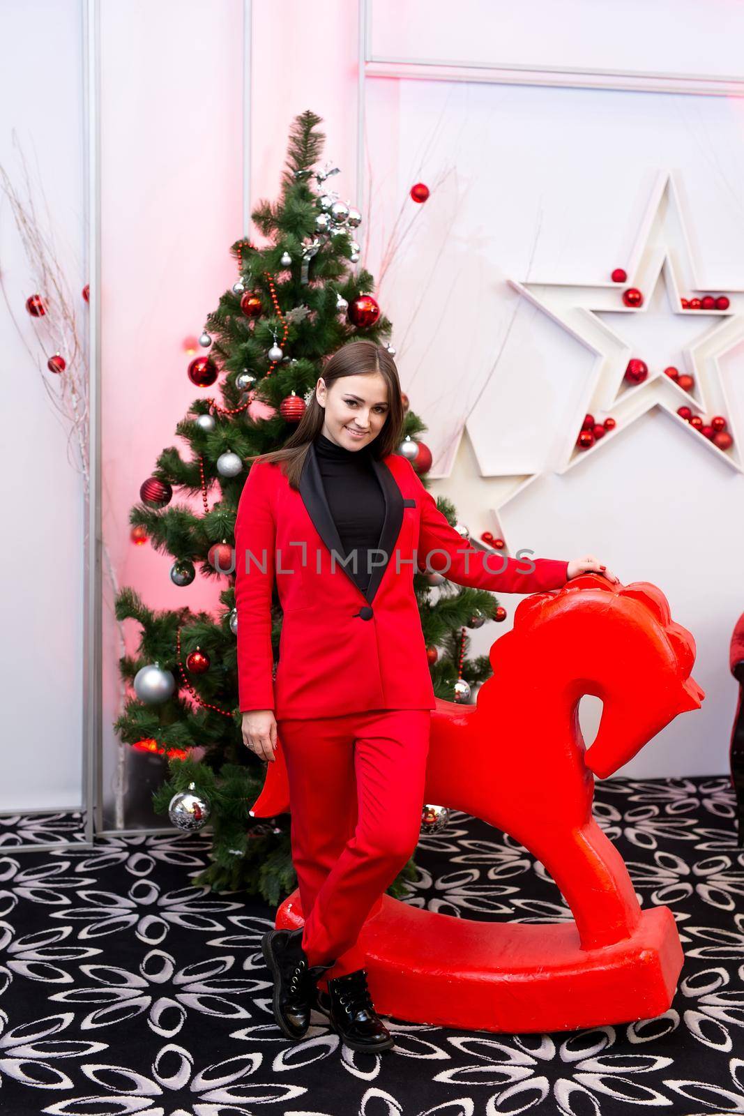 An elegant lady in red on the background of a Christmas tree and a horse. Happy New Year by StudioPeace