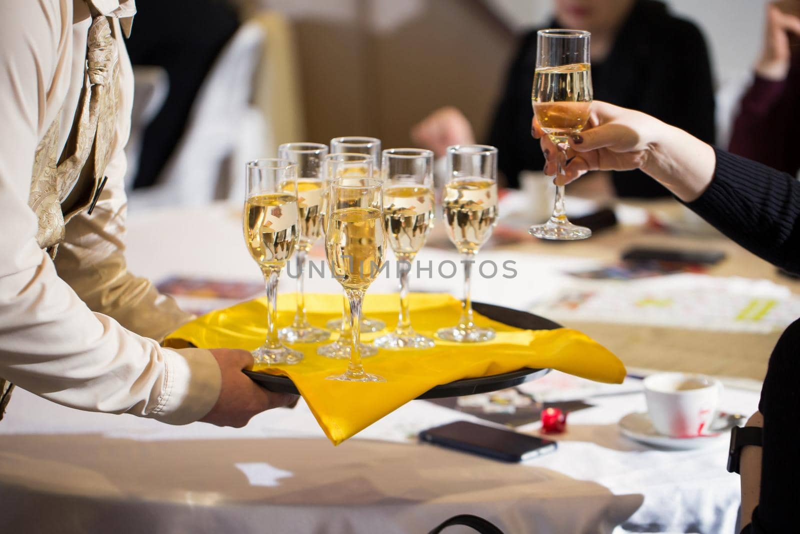 Waiter served champagne glasses on a tray in a fine dining restaurant and woman takes a glass. by StudioPeace