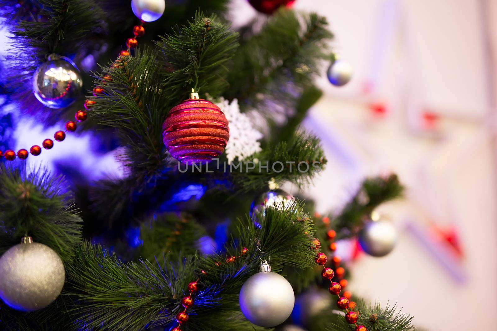 Decorated Christmas trees in close-up. Red and gold balls and illuminated garlands with flashlights.