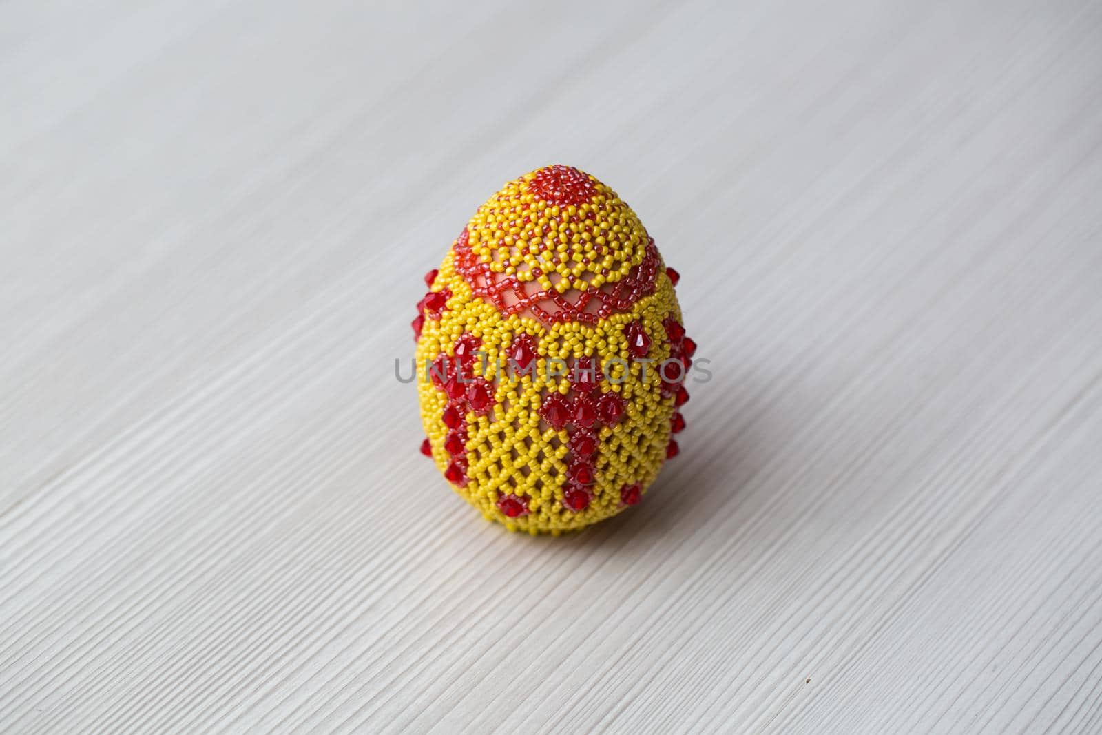Egg decorated with small beads on a white table. by StudioPeace