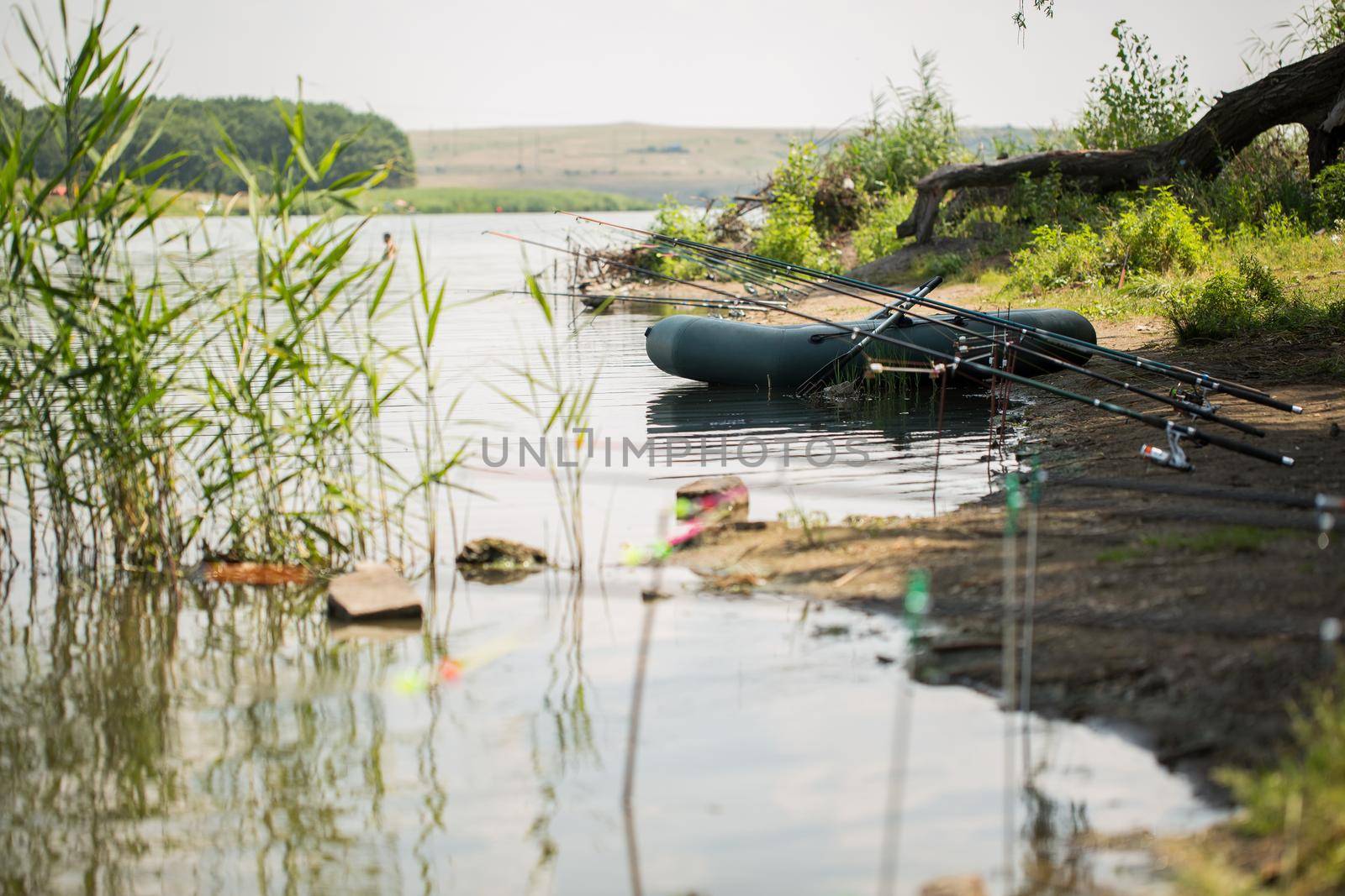 An inflatable boat, with boxes with fishing tackles, is standing on the water, pond, lake, near the shore on the background of tree, nature. Fishing background. boat with oars by StudioPeace
