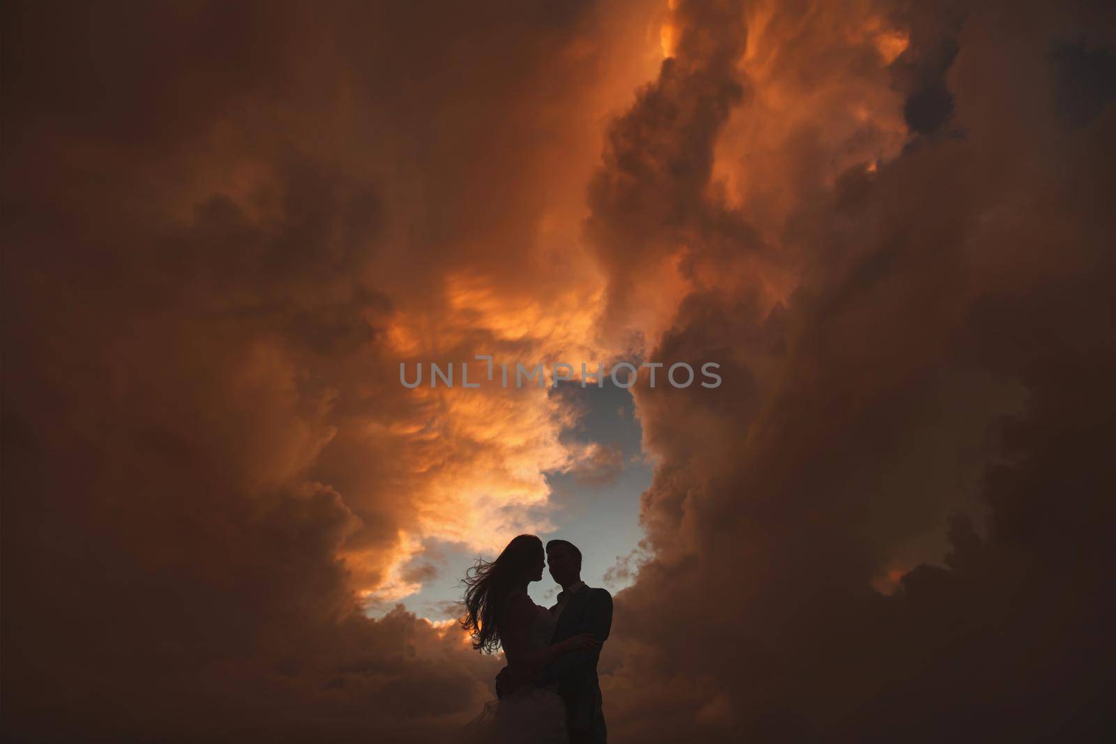 Silhouette of bride and groom at sunset on a background of clouds.