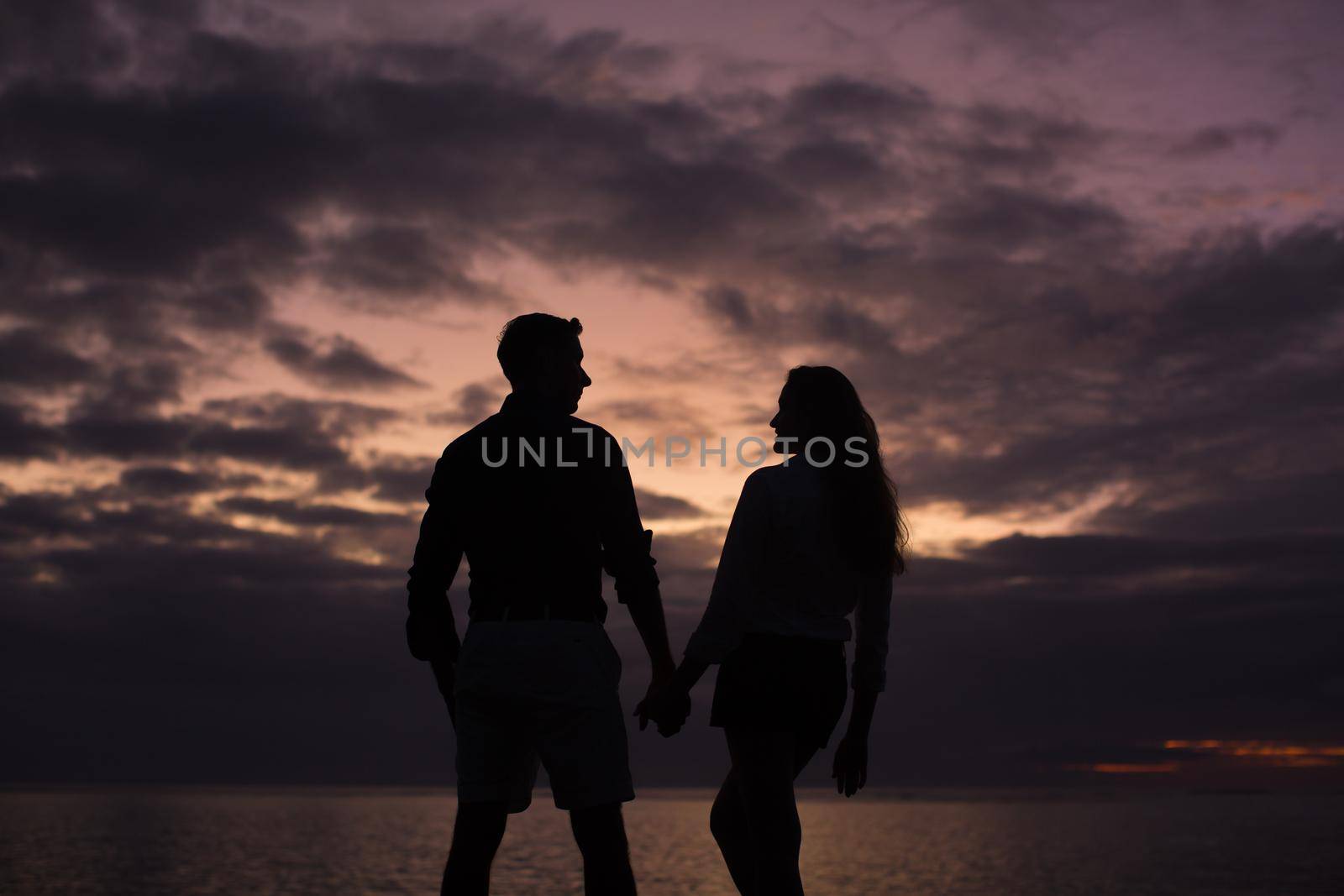 Silhouette of a young couple at sunset on the beach near the ocean. by StudioPeace