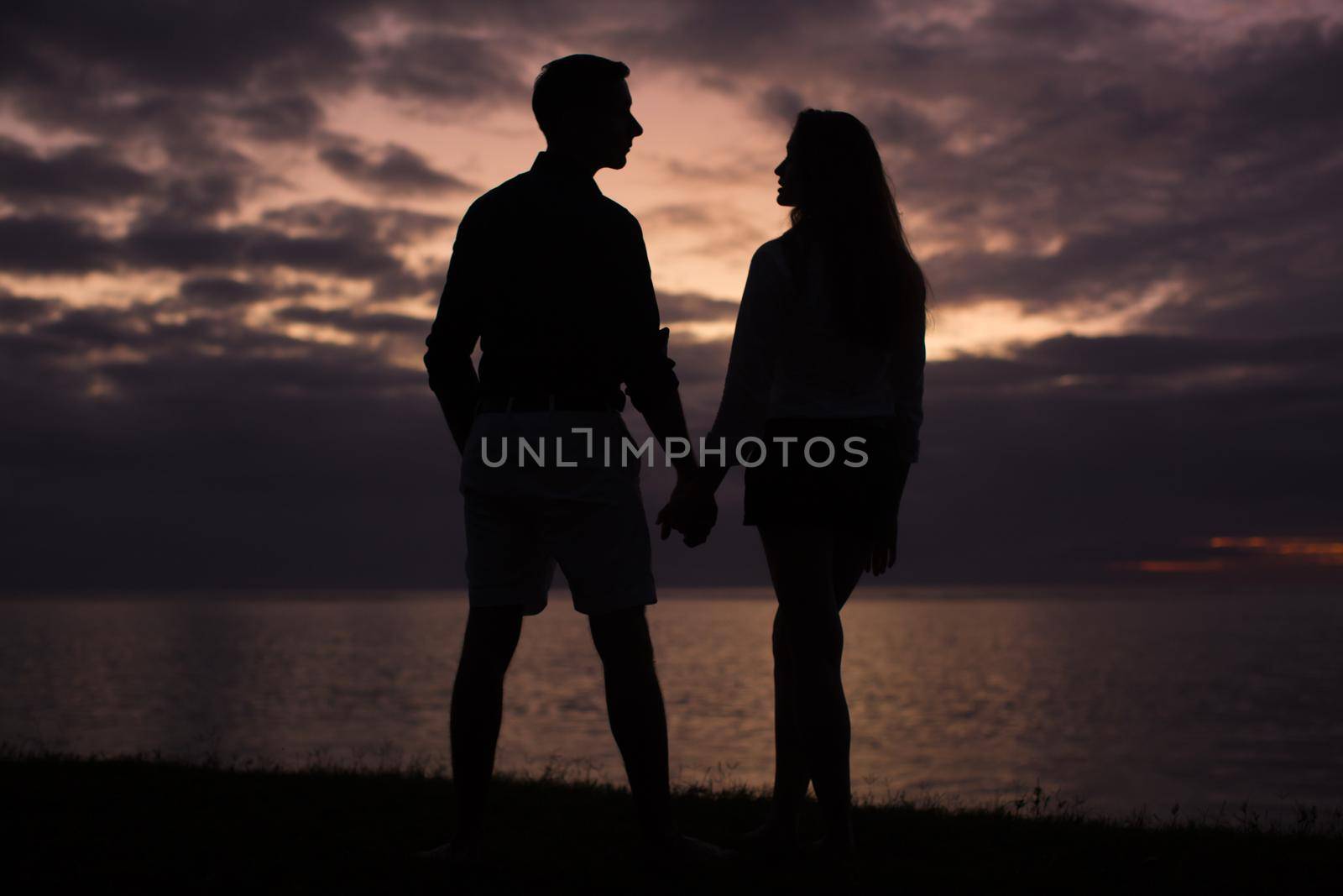 Silhouette of a young couple at sunset on the beach near the ocean. by StudioPeace