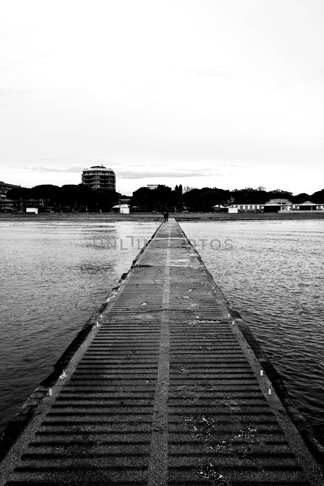 Monochrome shot of an old concrete jetty leading to the shore.