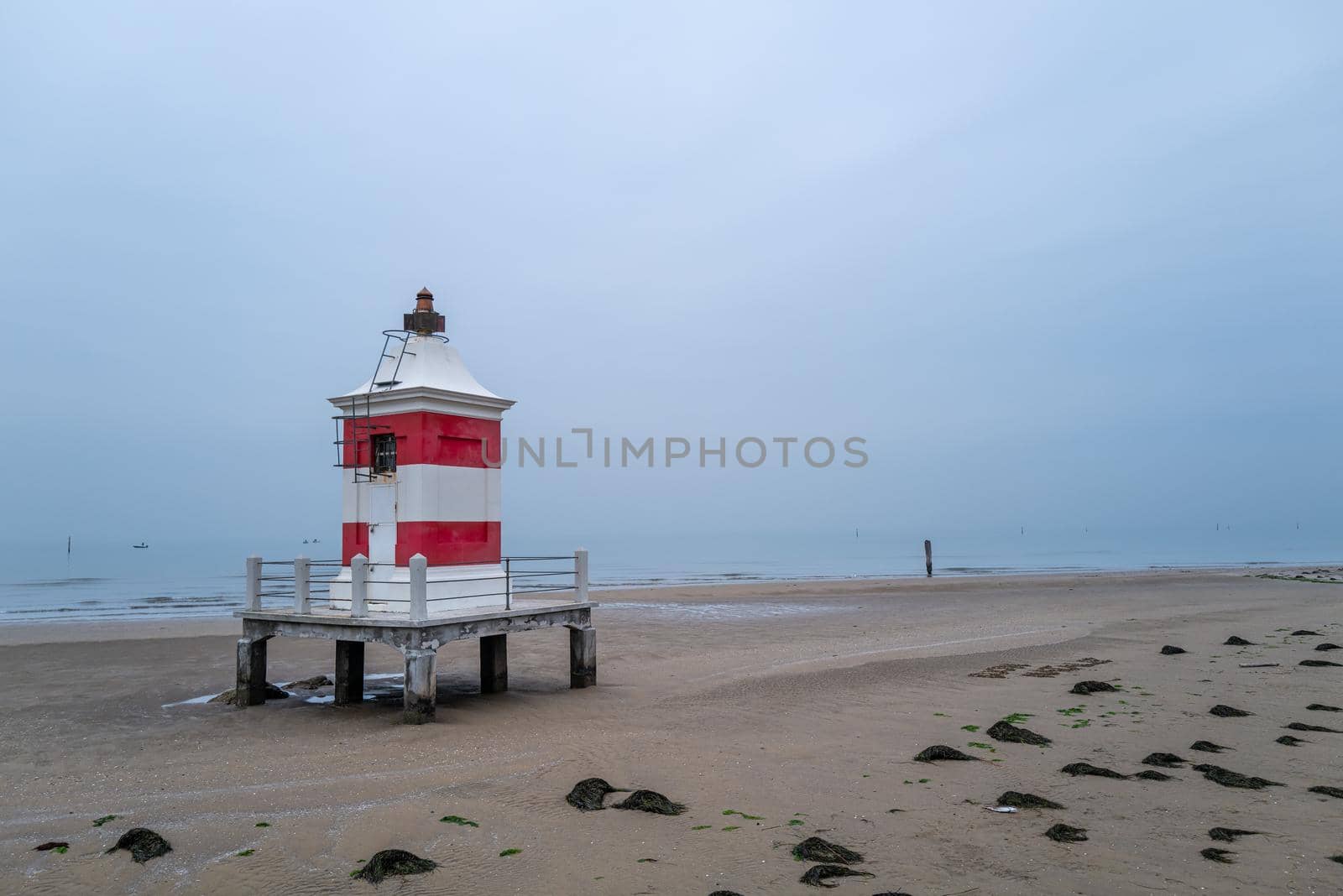 Small red white wooden lighthouse on wintry sandy beach without people.