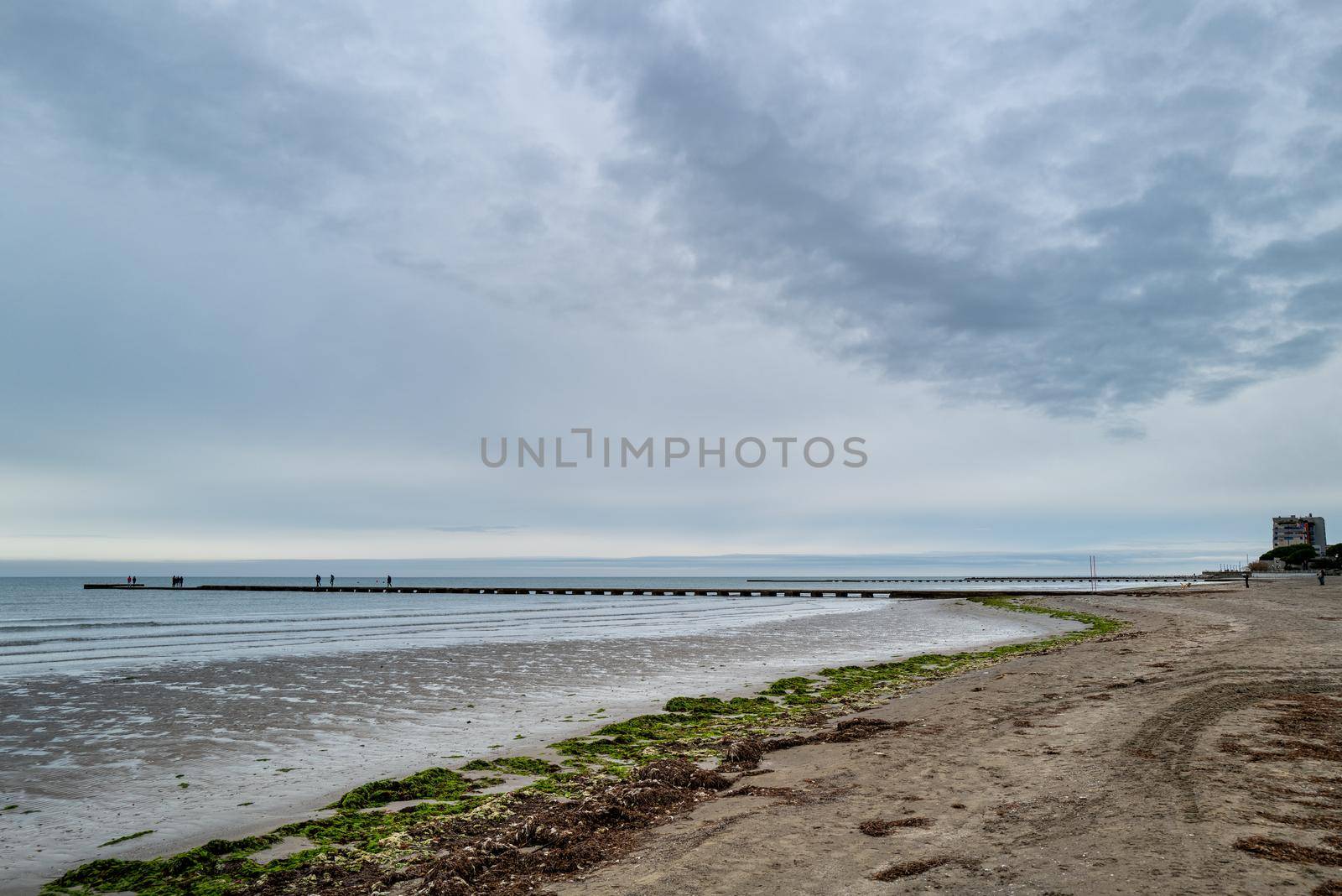 At the end of a deserted sandy beach, a jetty leads far out into the sea.