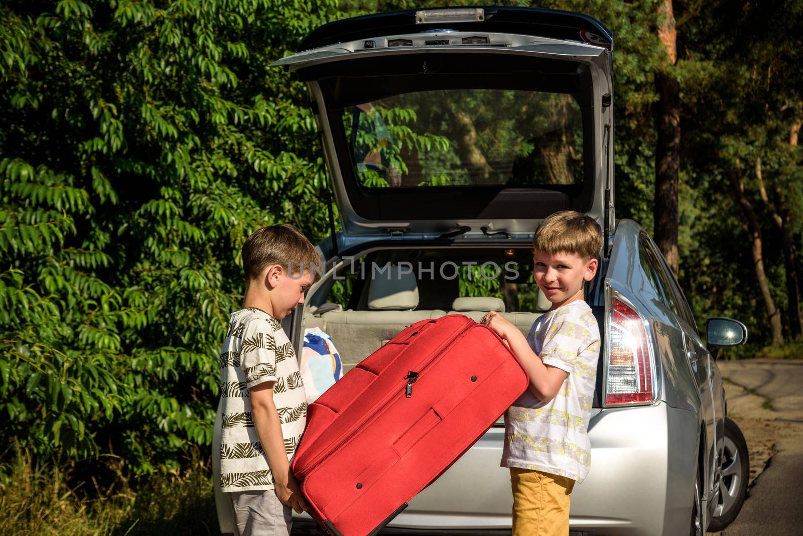Two adorable boys holding a suitcase going on vacations with their parents. Two kids looking forward for a road trip or travel. Family travel by car.