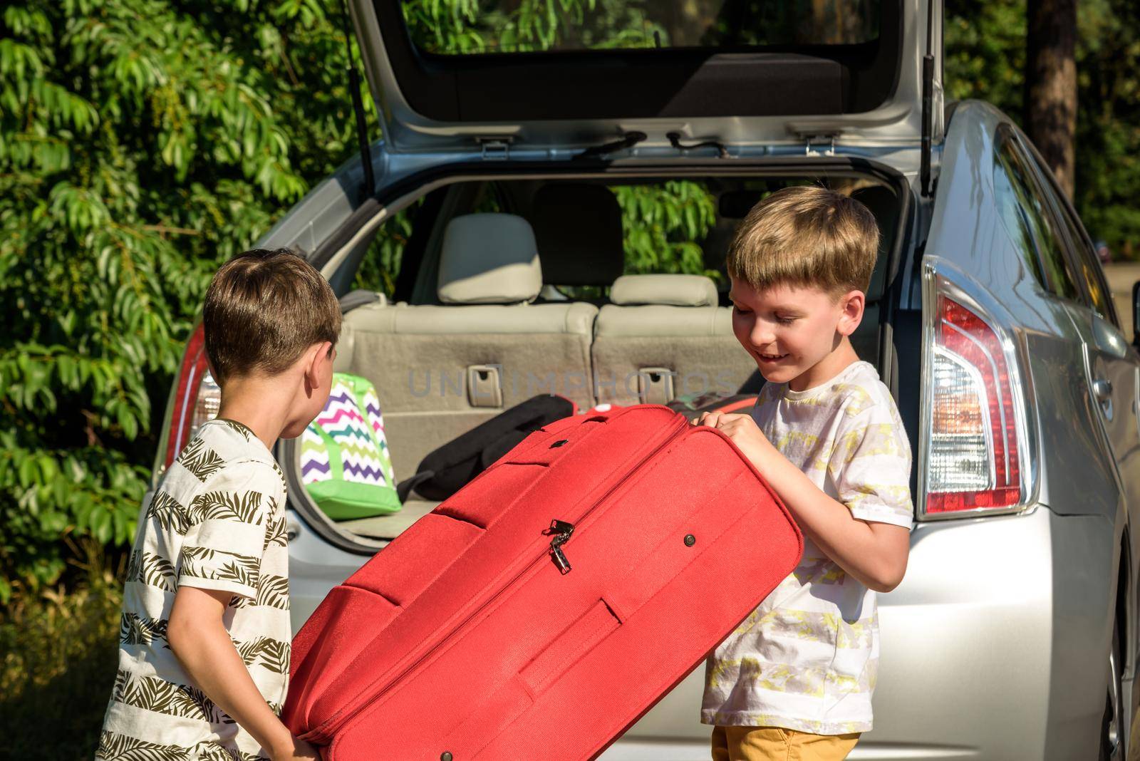 Two adorable boys holding a suitcase going on vacations with their parents. Two kids looking forward for a road trip or travel. Family travel by car.