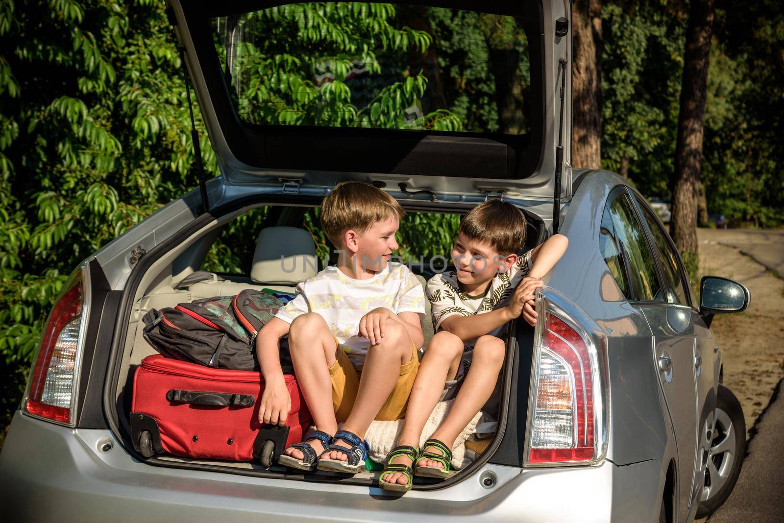 Two cute boys sitting in a car trunk before going on vacations with their parents. Two kids looking forward for a road trip or travel. Summer break at school. Family travel by car.