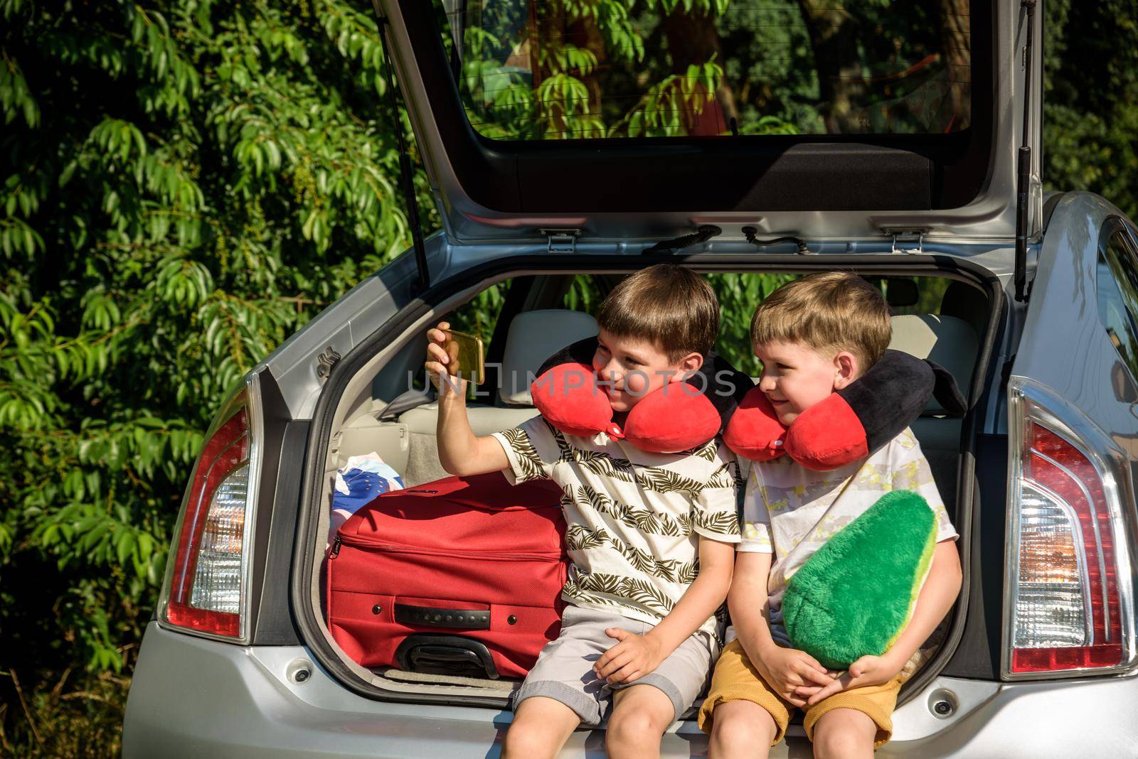 Two adorable little kids boy sitting in car trunk just before leaving for summer vacation. Sibling brothers making selfie on smartphone. Happy family going on long journey by Kobysh