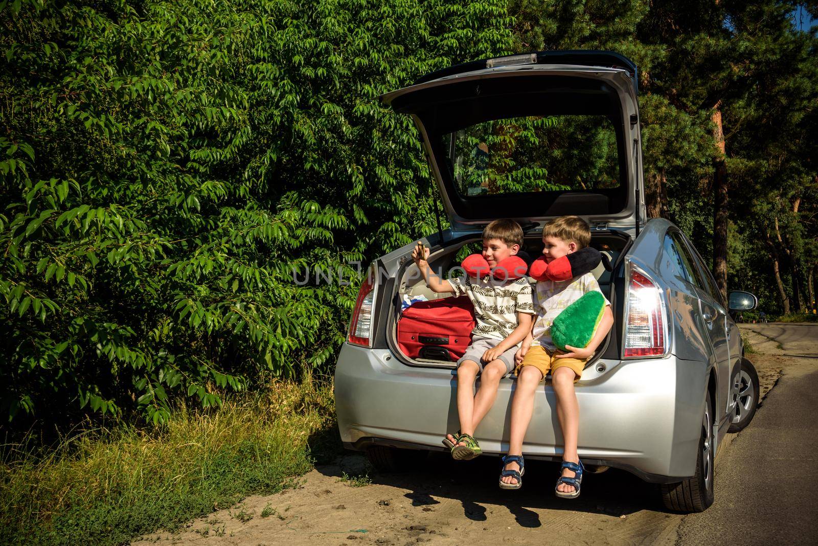 Two adorable little kids boy sitting in car trunk just before leaving for summer vacation. Sibling brothers making selfie on smartphone. Happy family going on long journey by Kobysh