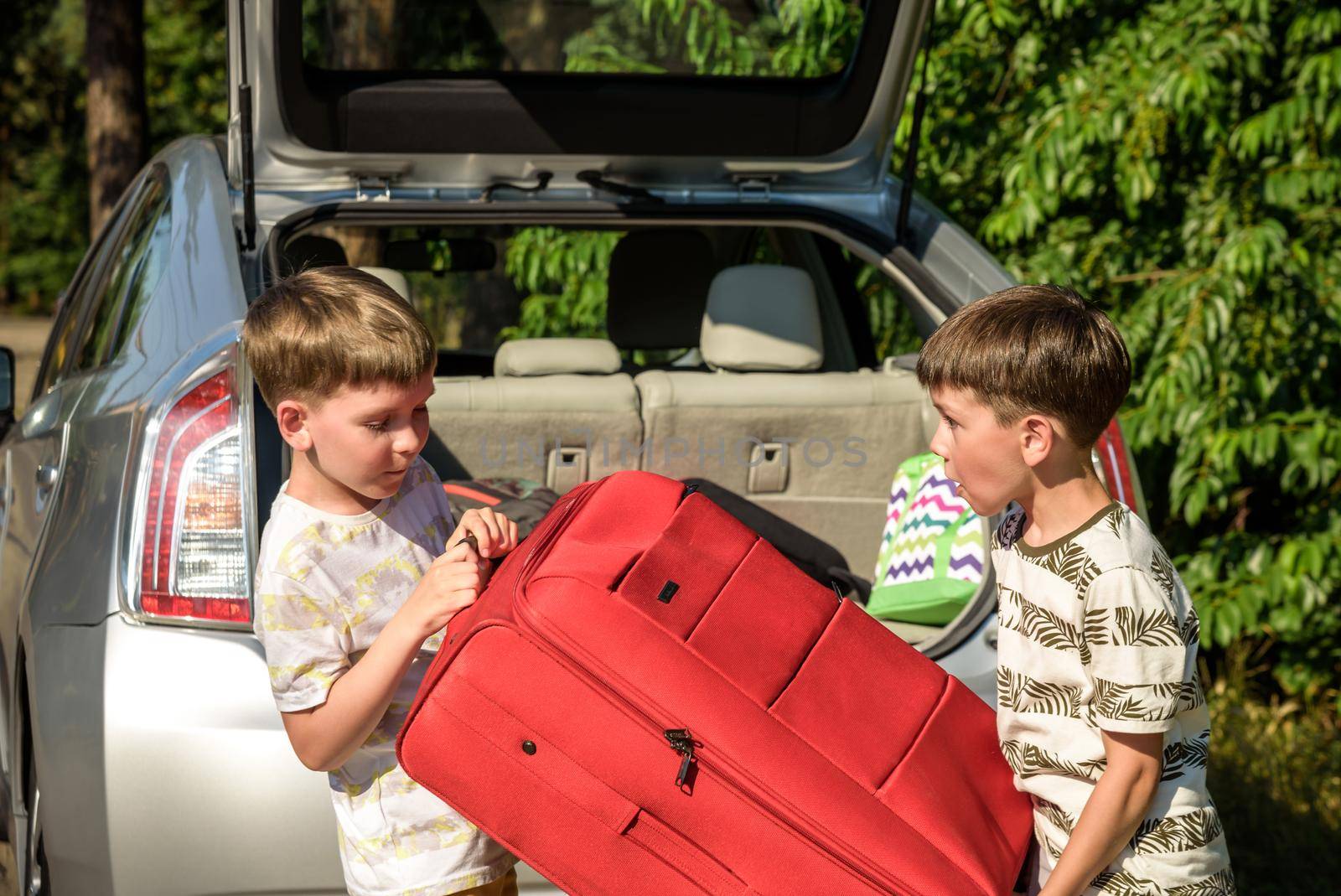 Two adorable boys holding a suitcase going on vacations with their parents. Two kids looking forward for a road trip or travel. Family travel by car.