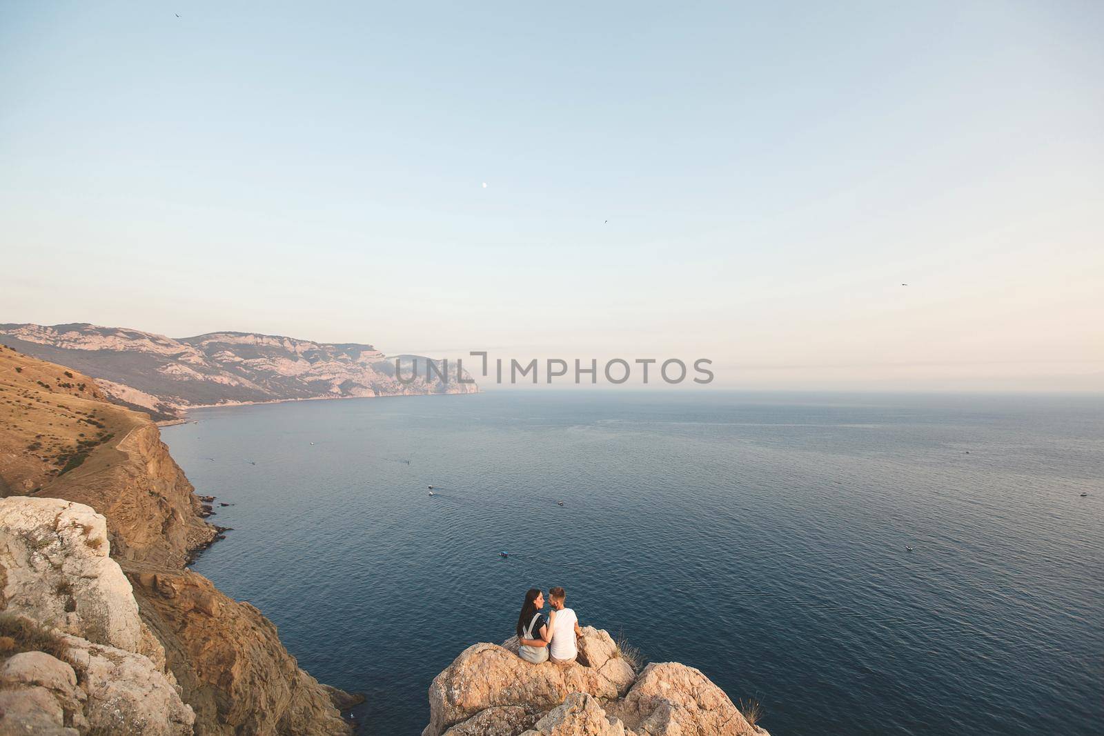 Guy and girl, on the edge of the cliff against the backdrop of mountains and ocean