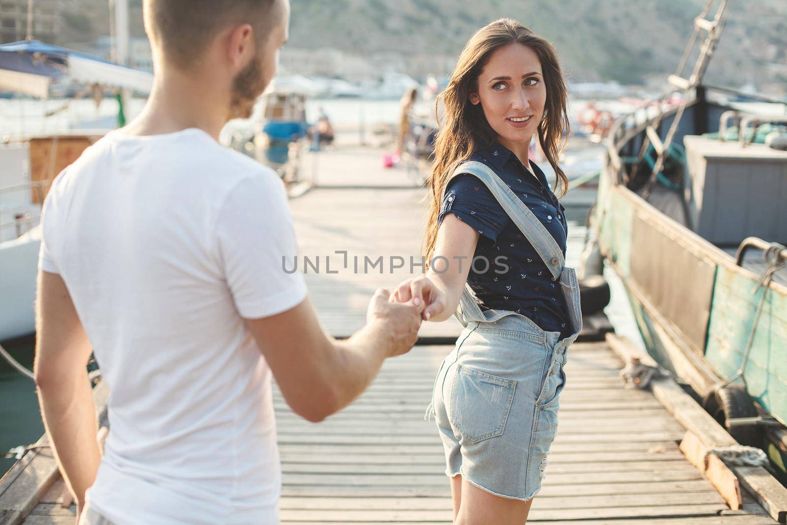 Lovers, boy and girl, walk on a wooden pier and hold hands.