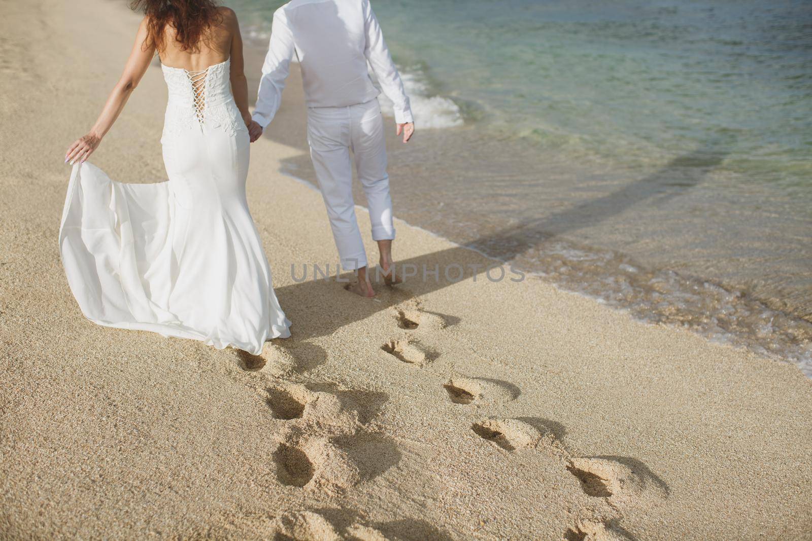 The bride and groom walk hand in the sand. footprints in the sand near the ocean
