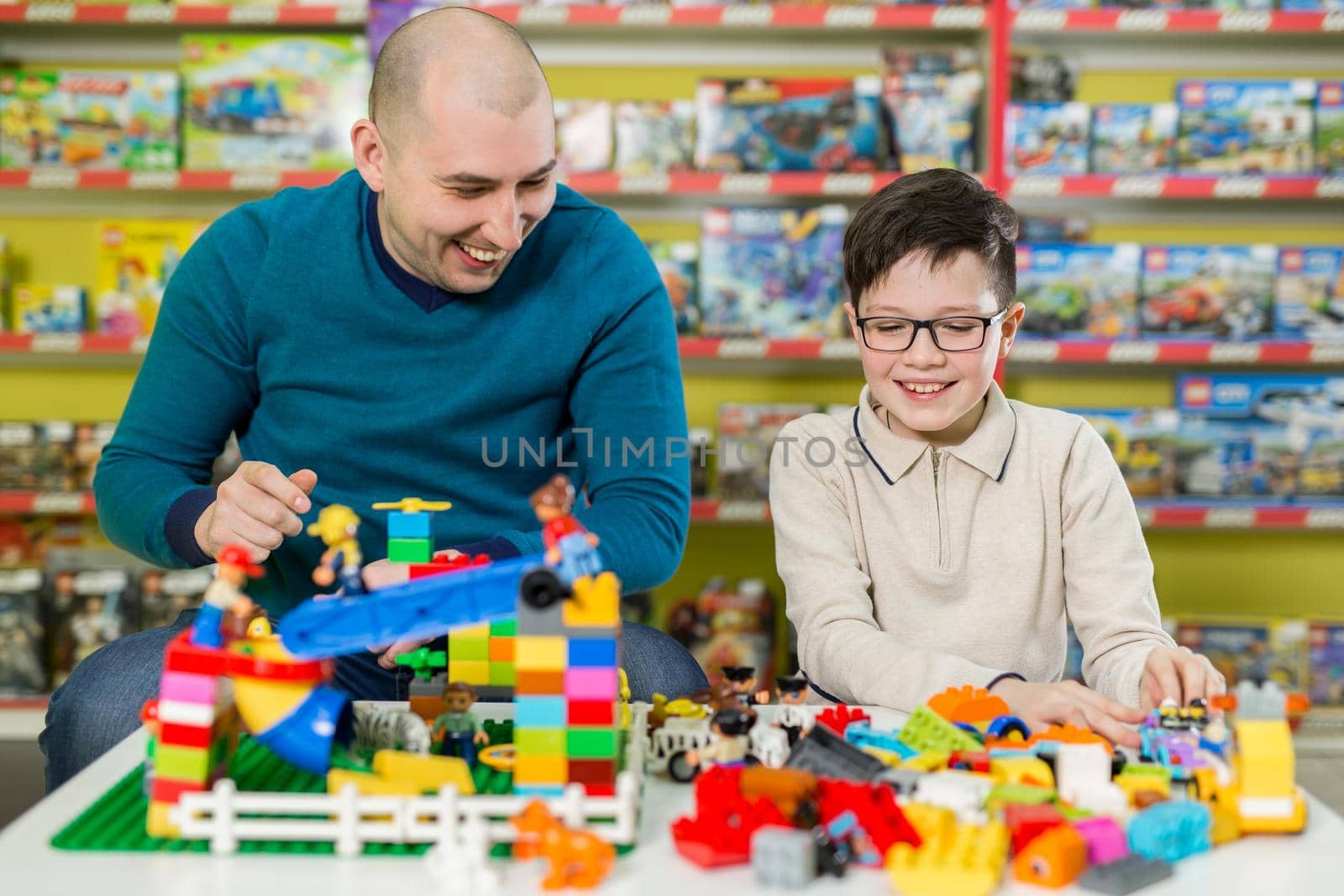 Father and son with happy faces create colorful constructions of toy bricks. Dad and kid build of plastic blocks. Family and childhood concept by StudioPeace