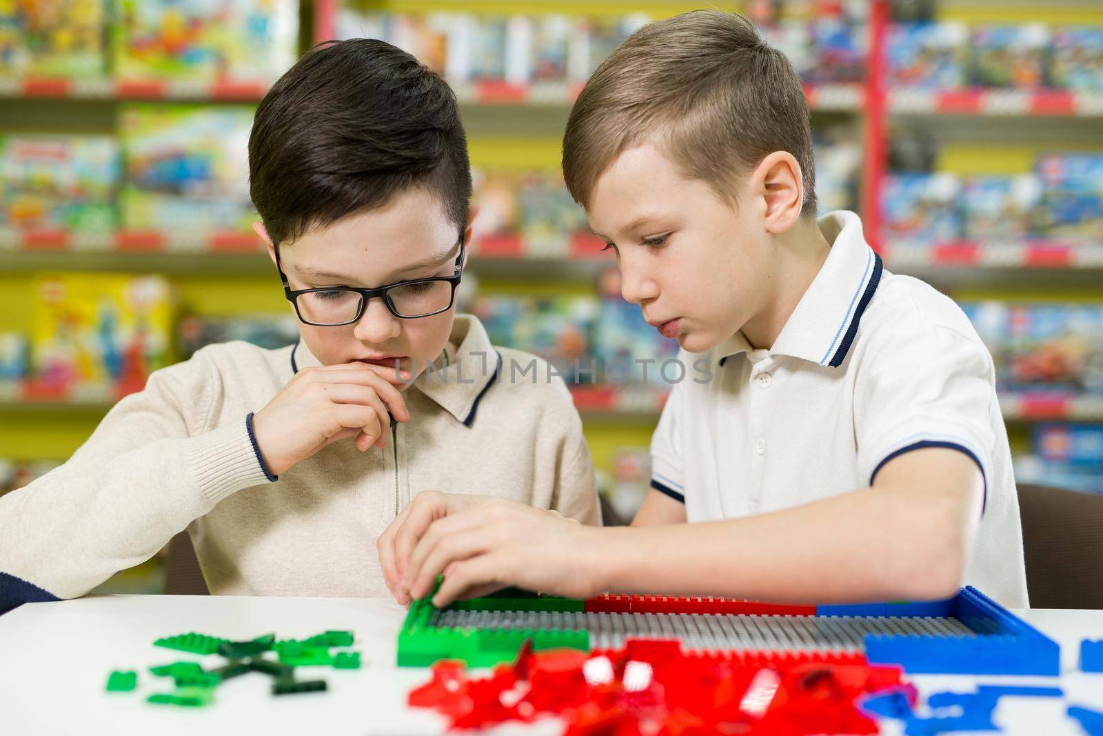 Children play in the designer at the table. Two boys play together with colored plastic blocks in the gaming center, school.