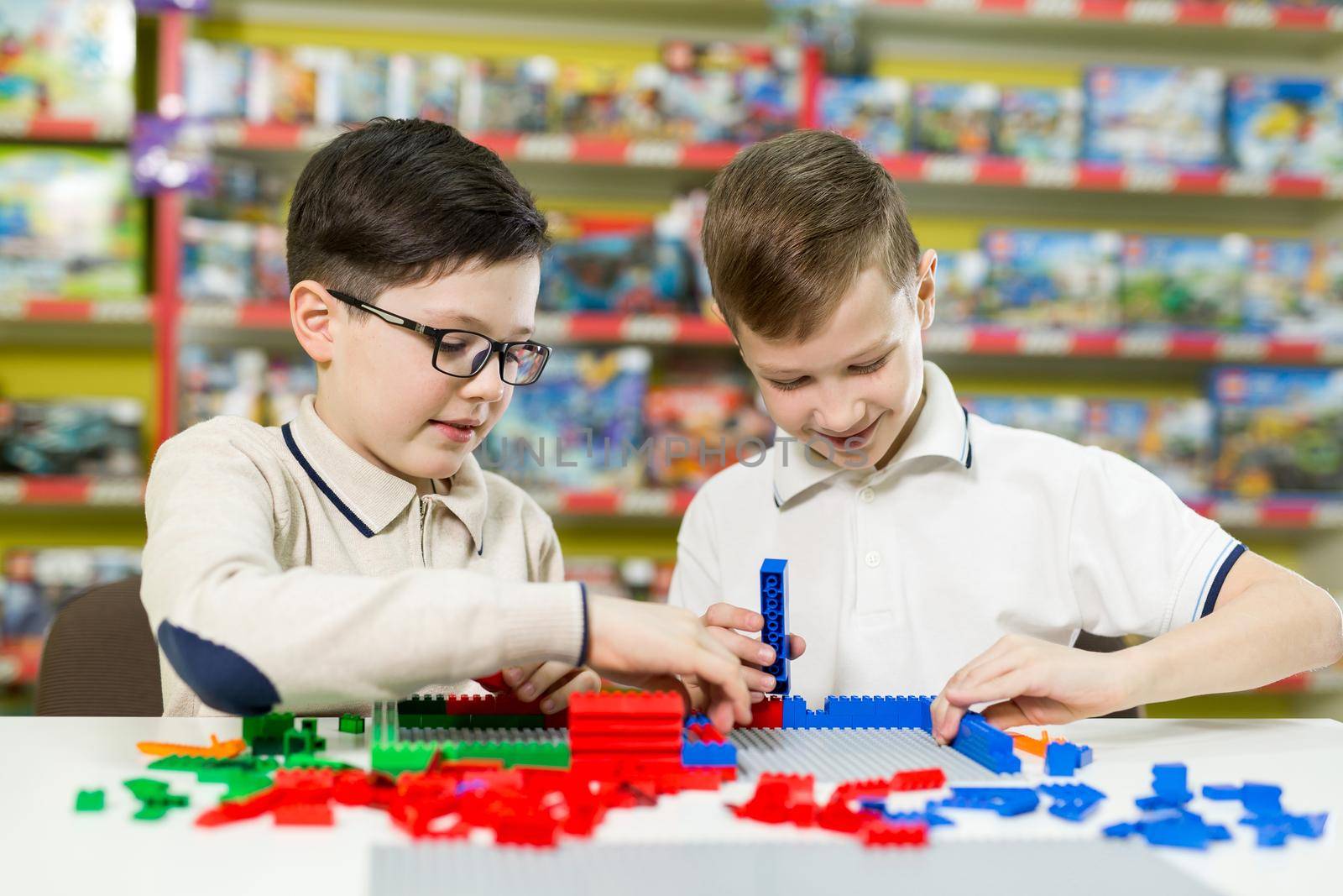 Children play in the designer at the table. Two boys play together with colored plastic blocks in the gaming center, school.