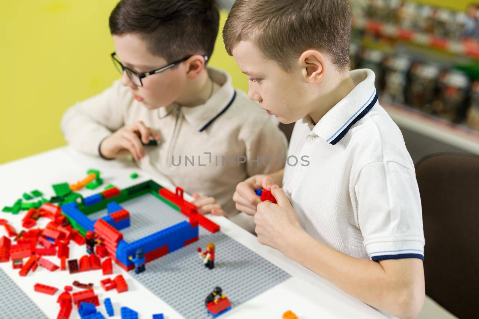 Children play in the designer at the table. Two boys play together with colored plastic blocks in the gaming center, school.