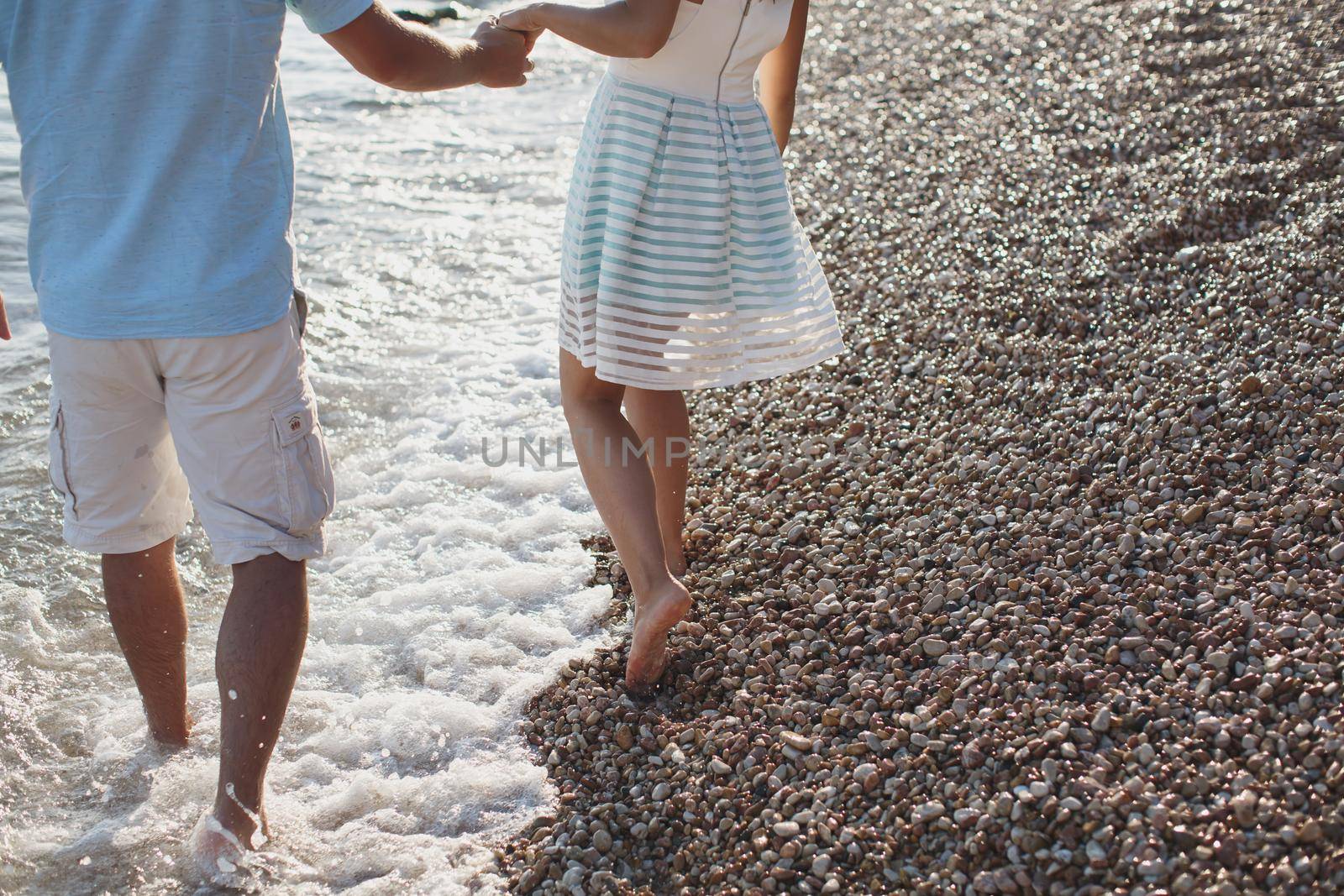 Couple holding hands walking on the pebbles near the sea