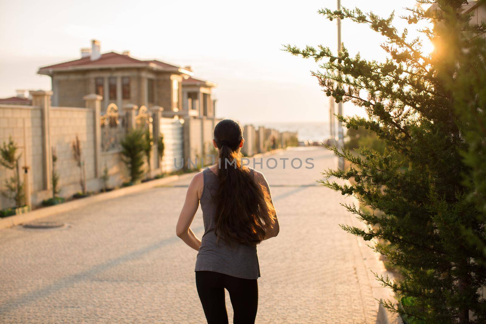 Young sporty woman running in the city at sunset. Rear view sporty girl working on the waterfront. by StudioPeace