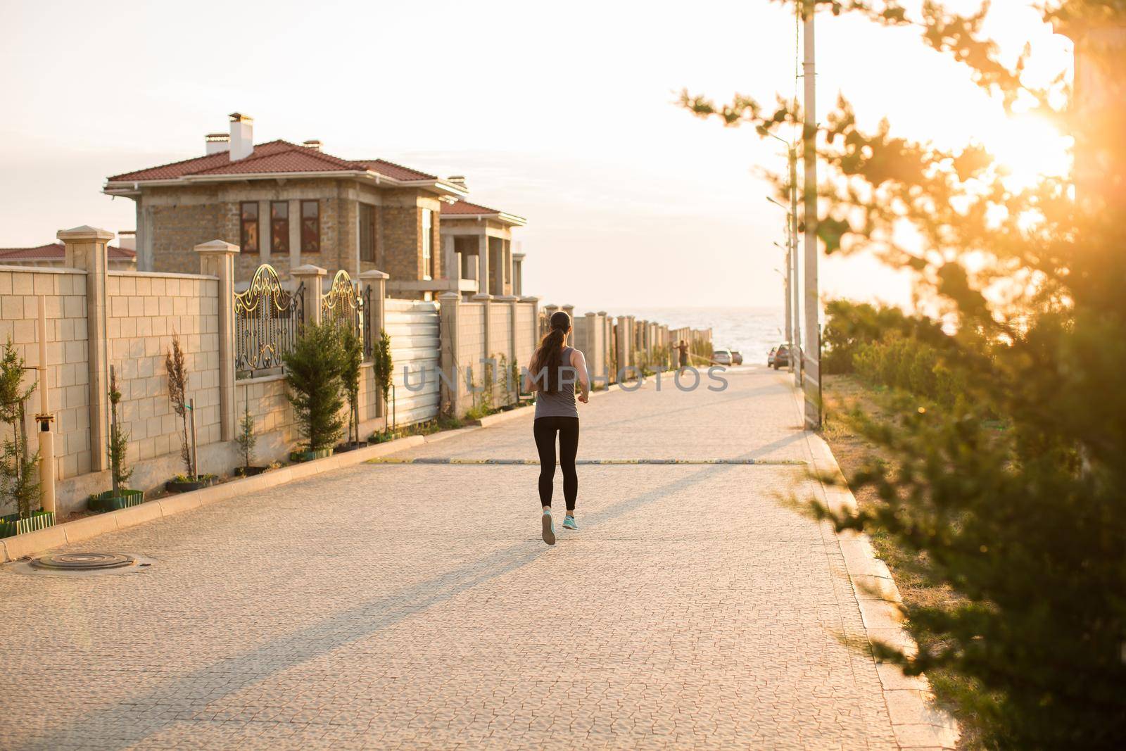 Young sporty woman running in the city at sunset. Rear view sporty girl working on the waterfront. by StudioPeace