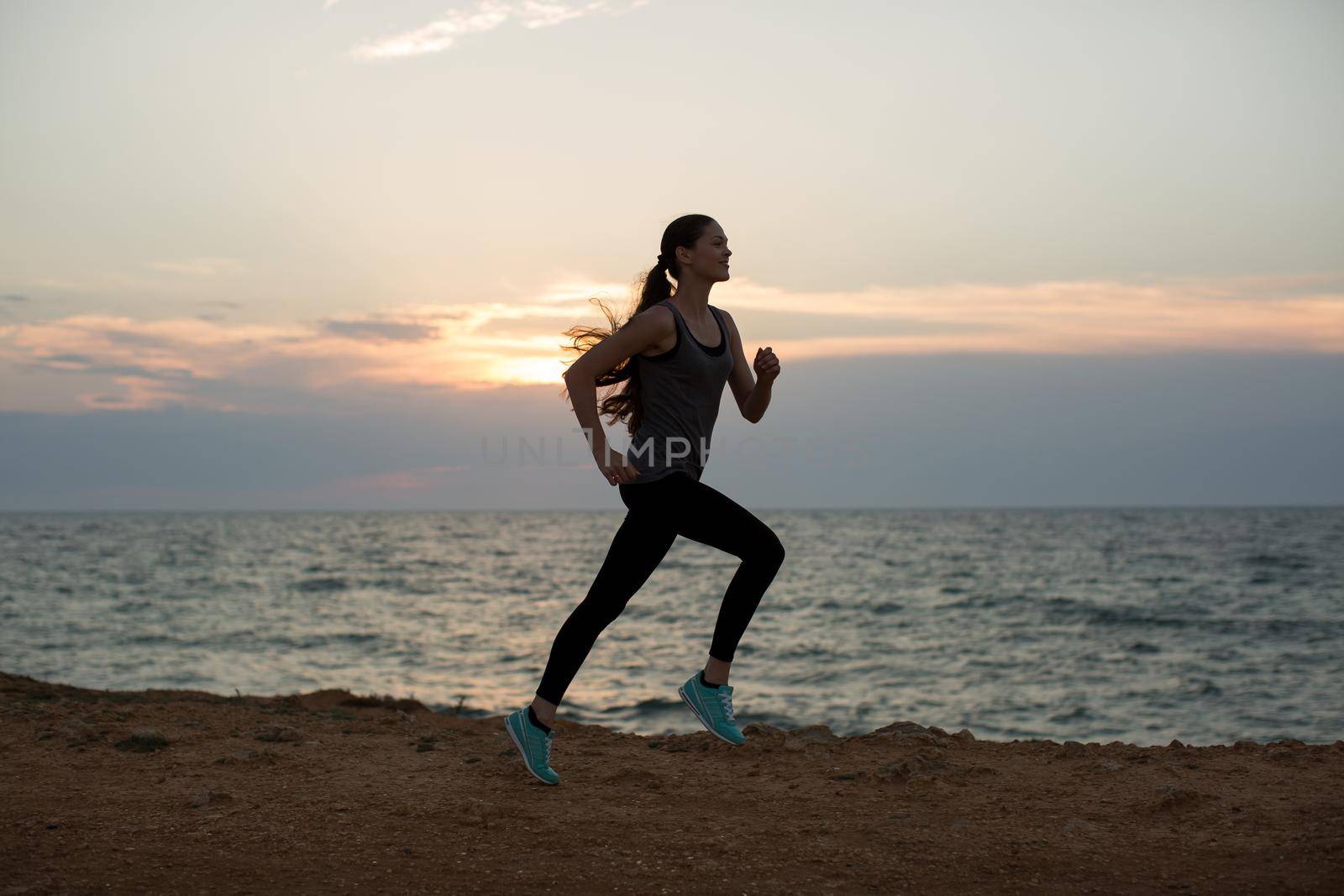 Silhouette of a young girl running along the beach of the sea during an amazing sunset.