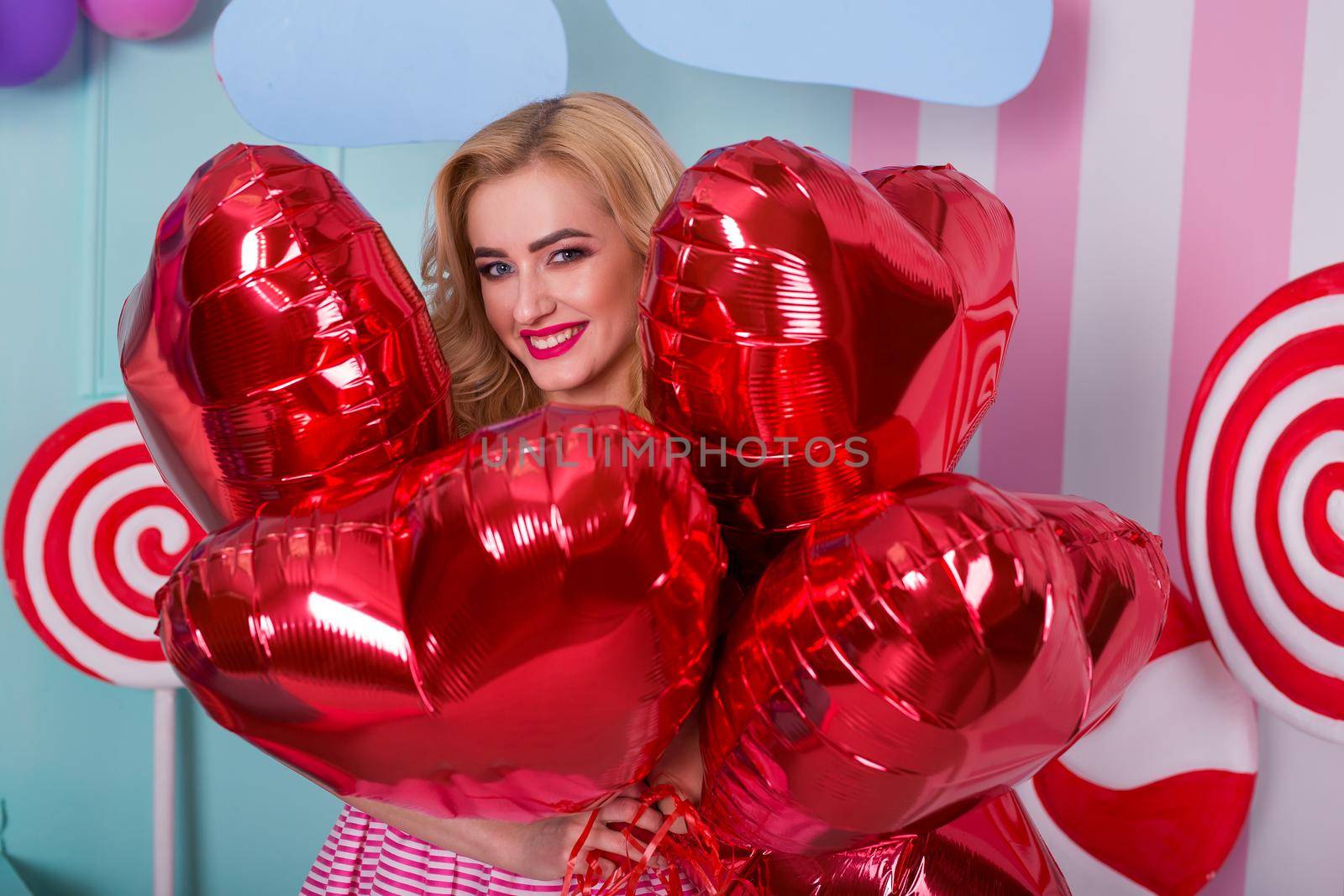 Fashion portrait of young woman in pink dress with an air balloons, candy on a colorful background.