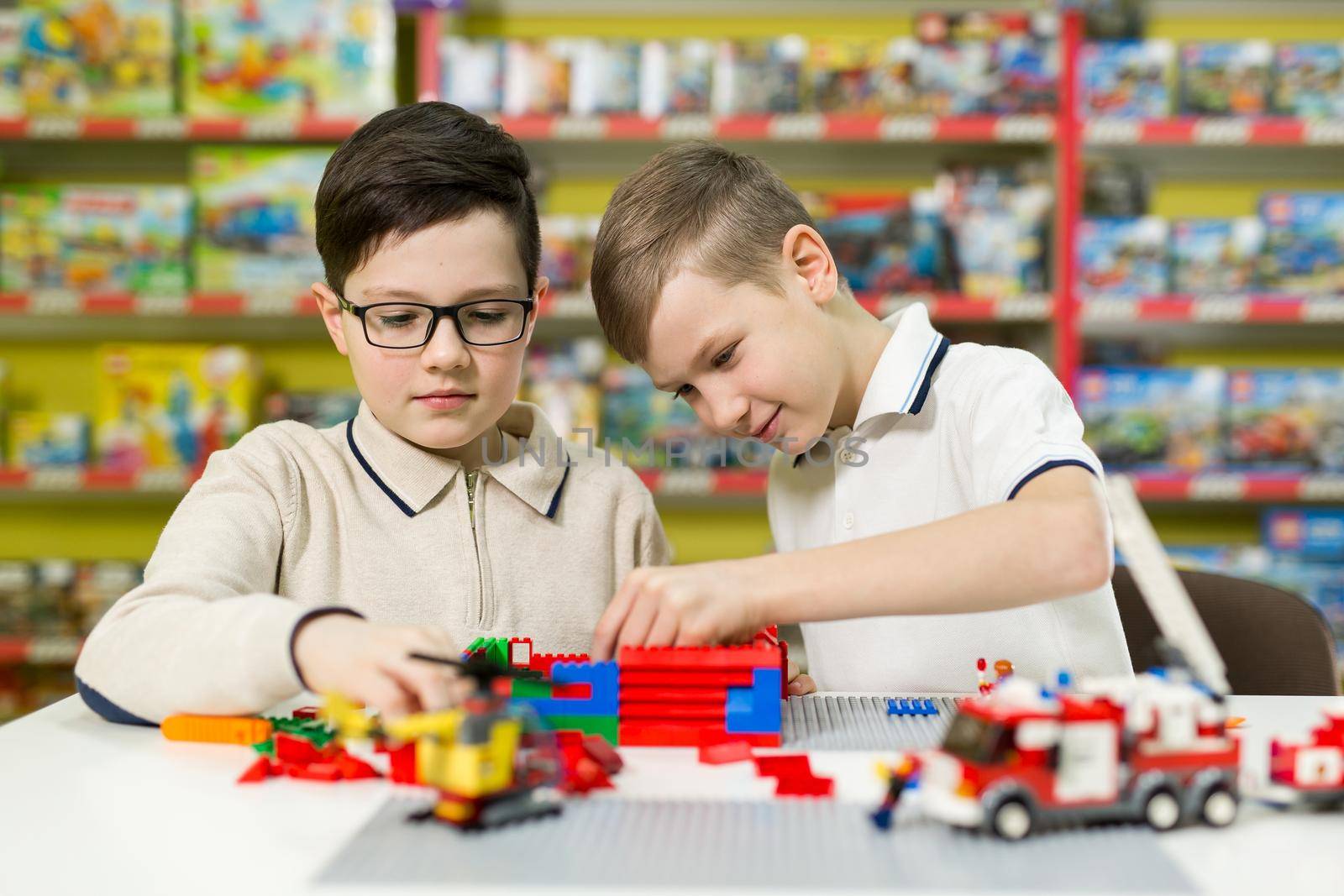 Children play in the designer at the table. Two boys play together with colored plastic blocks in the gaming center, school by StudioPeace