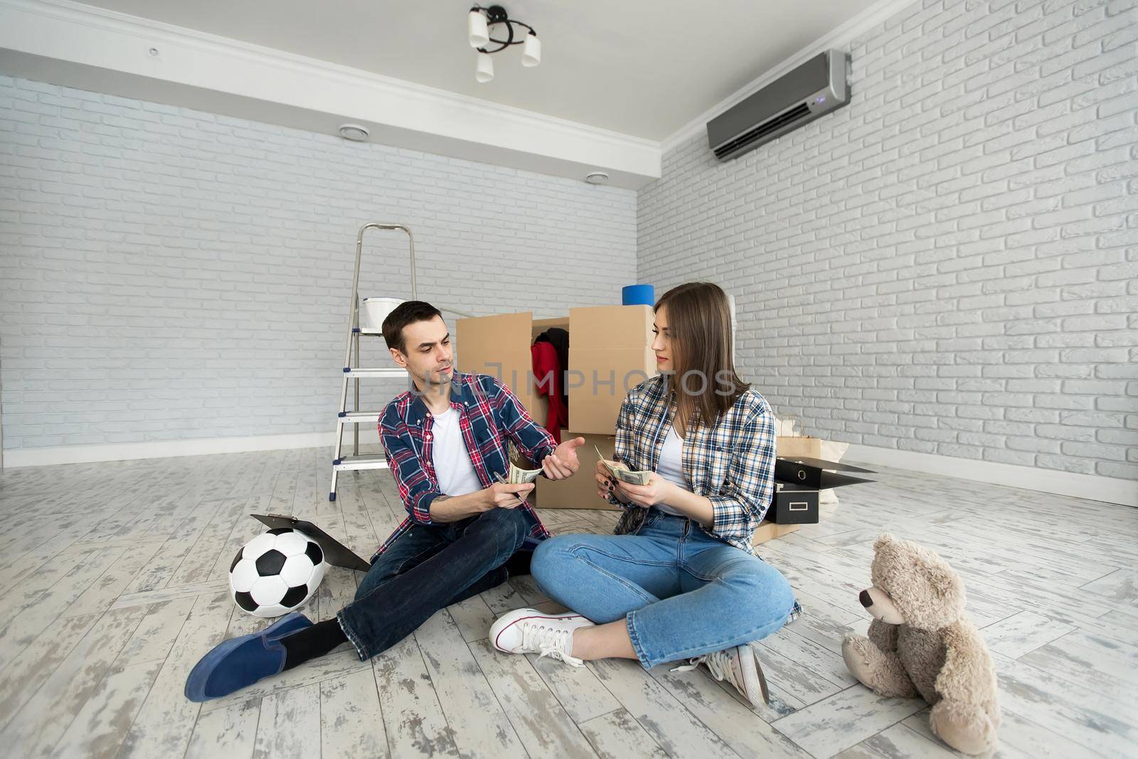 Young couple counting money while sitting on floor in new apartment. by StudioPeace