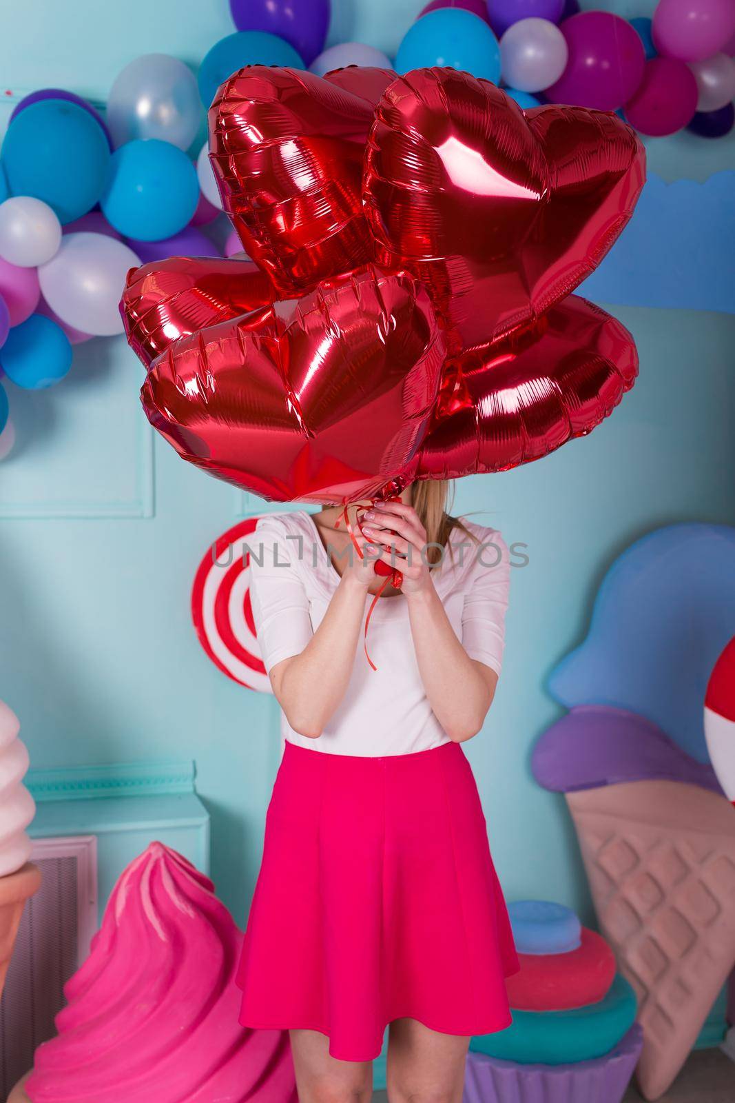 Fashion portrait of young woman in pink dress with an air balloons, candy on a colorful background.