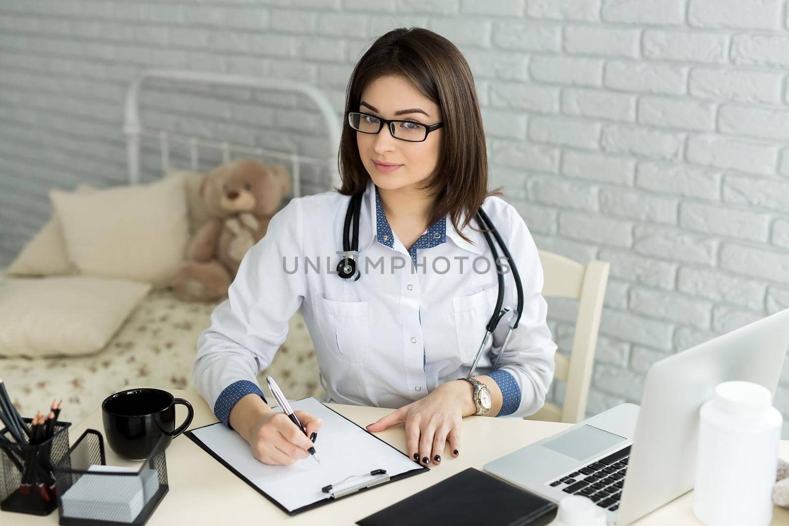 Portrait of cheerful happy female doctor sitting at her workplace. by StudioPeace