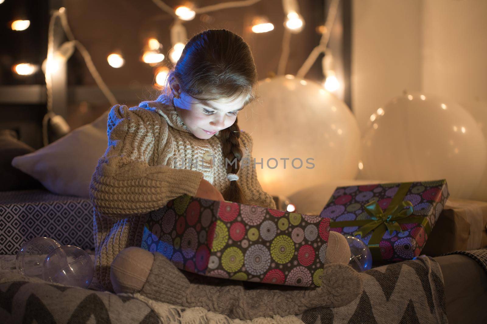 Beautiful little girl opens a magical Christmas gift in the cozy interior of the house. New year. by StudioPeace