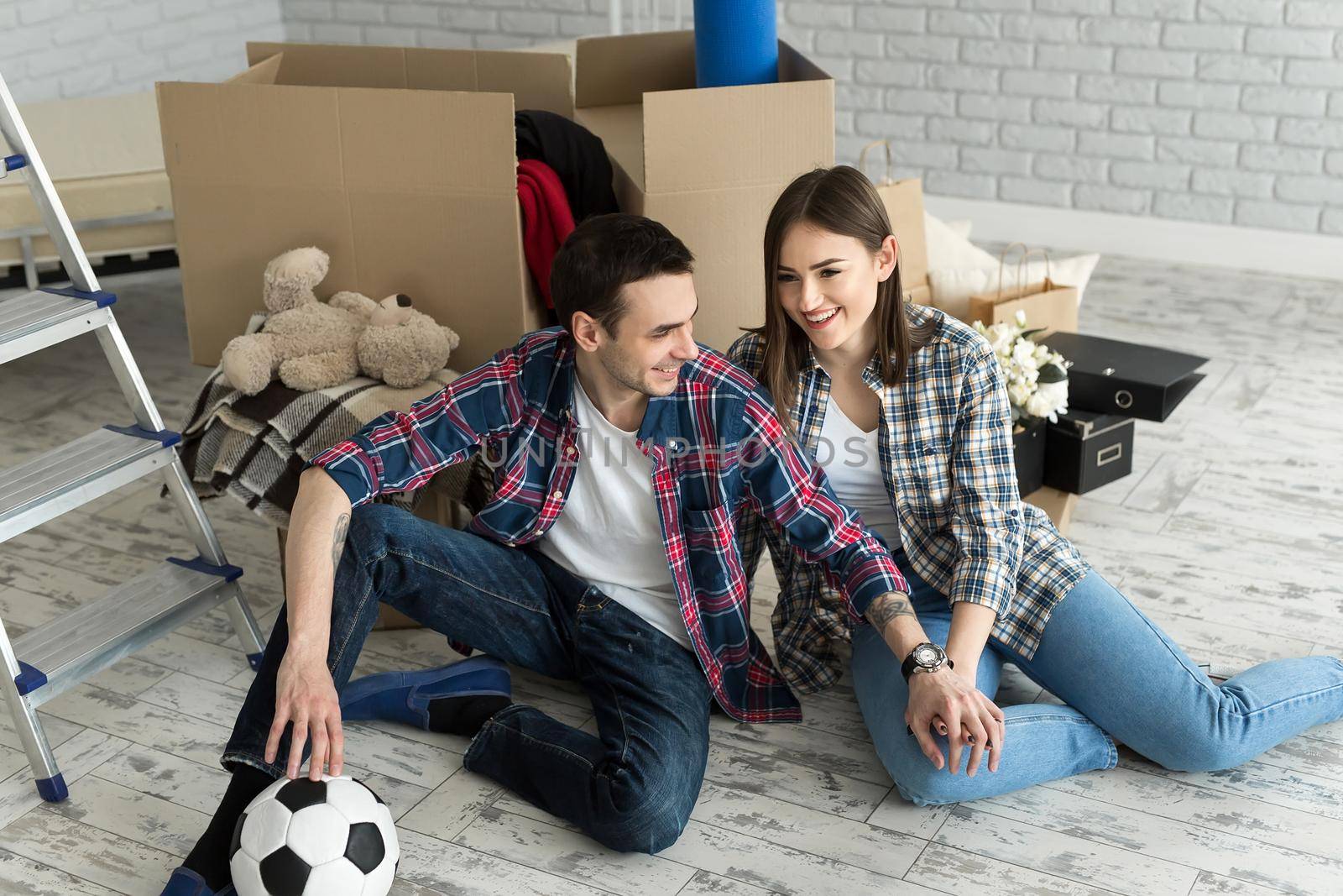 Young couple in a new home relaxing on the background of big boxes. Concept housewarming, began living together by StudioPeace