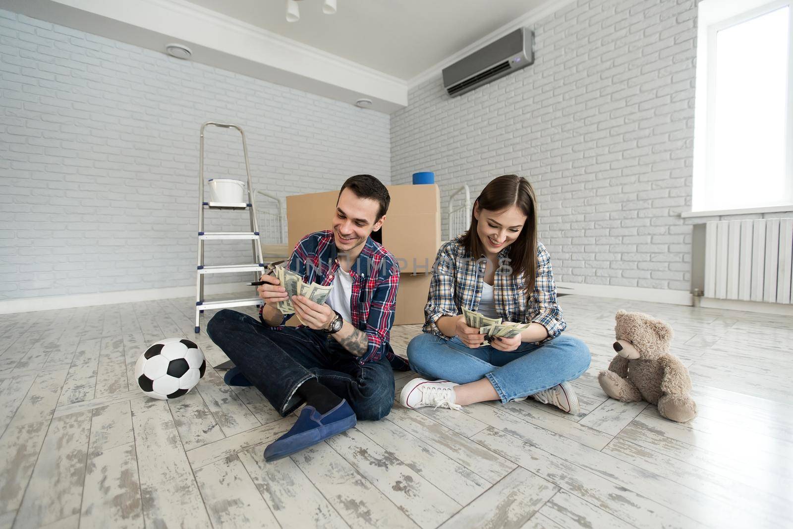 Young couple counting money while sitting on floor in new apartment. by StudioPeace