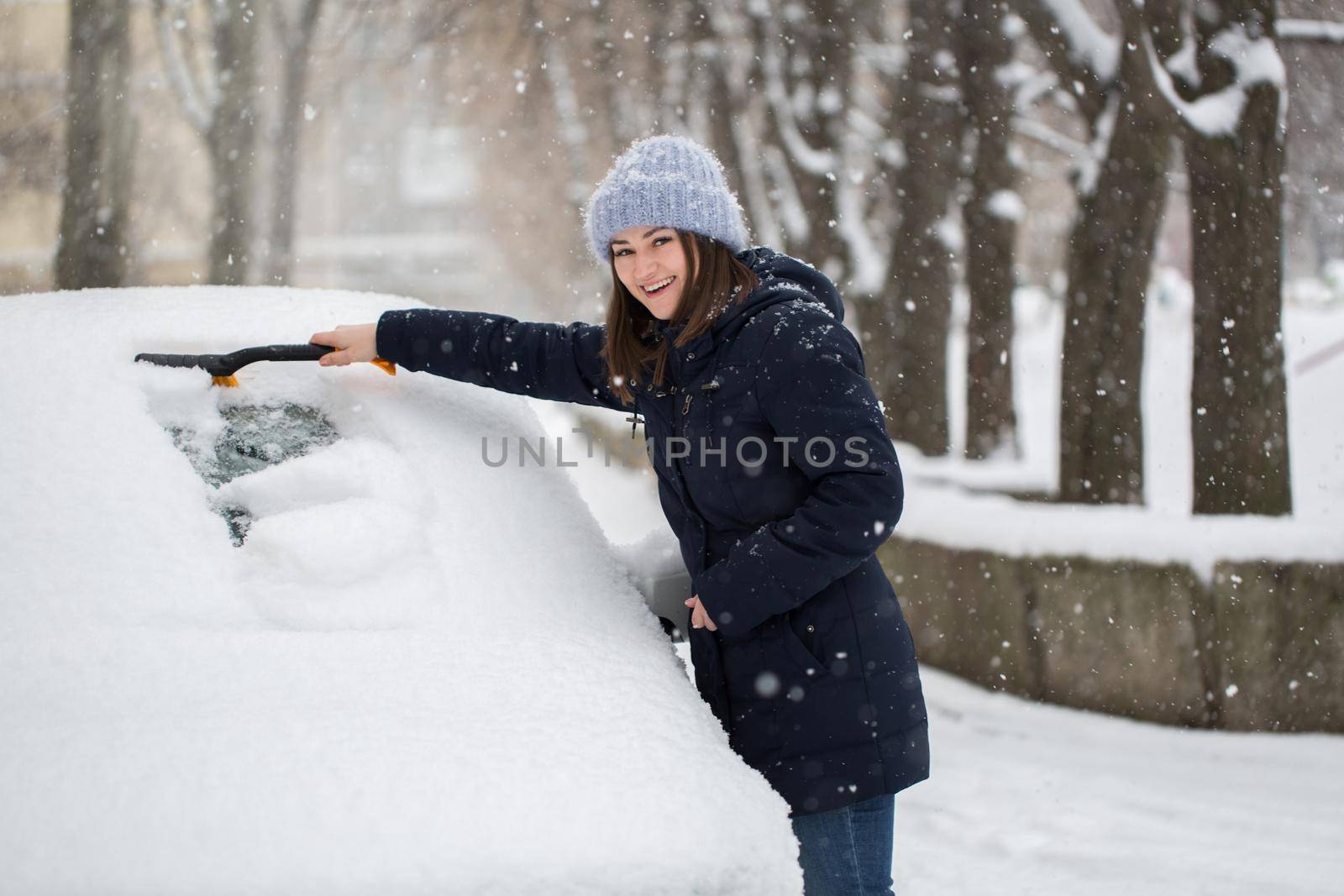 A woman removes snow from the windshield of a car. by StudioPeace