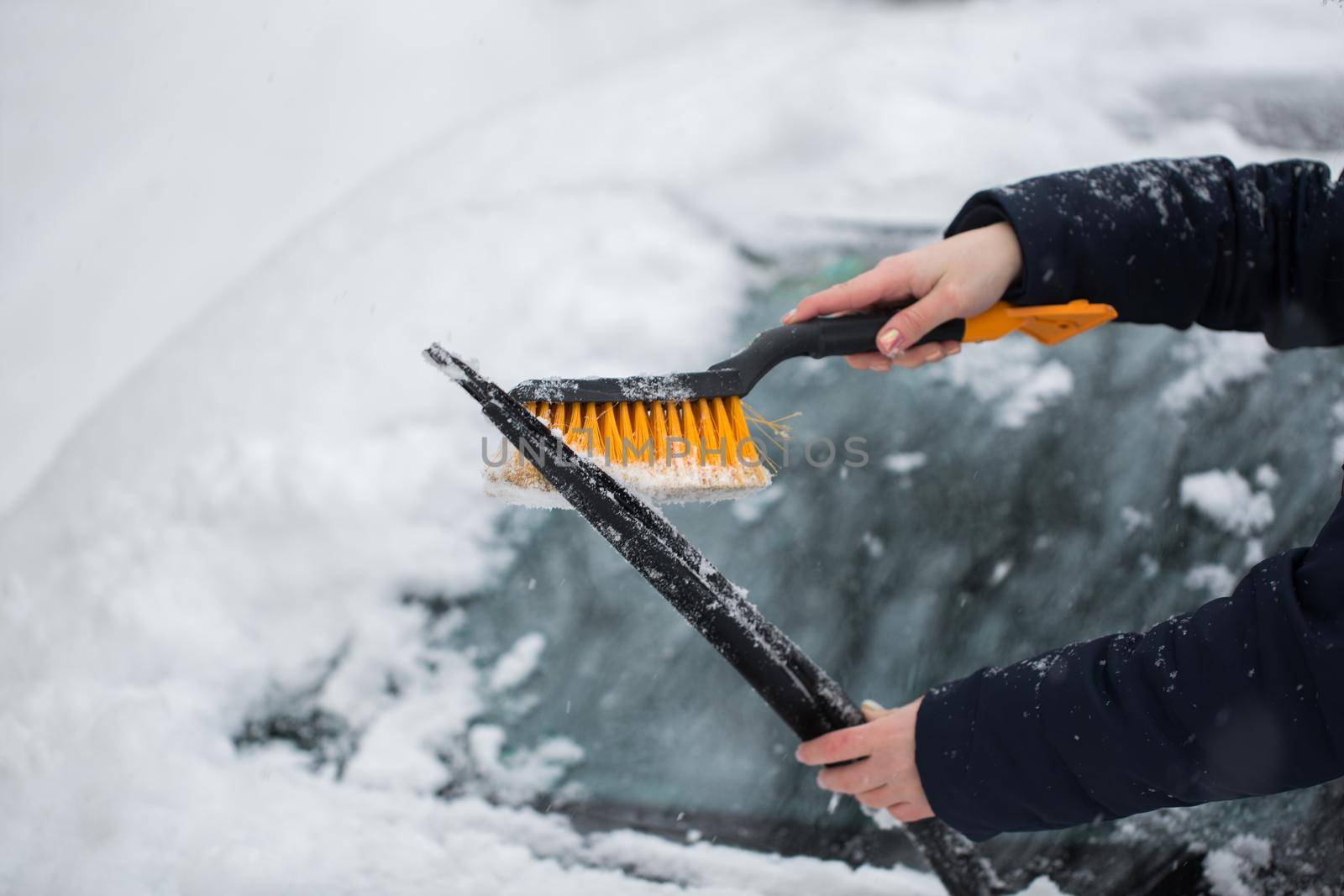 Woman cleaning snow from the car in the winter