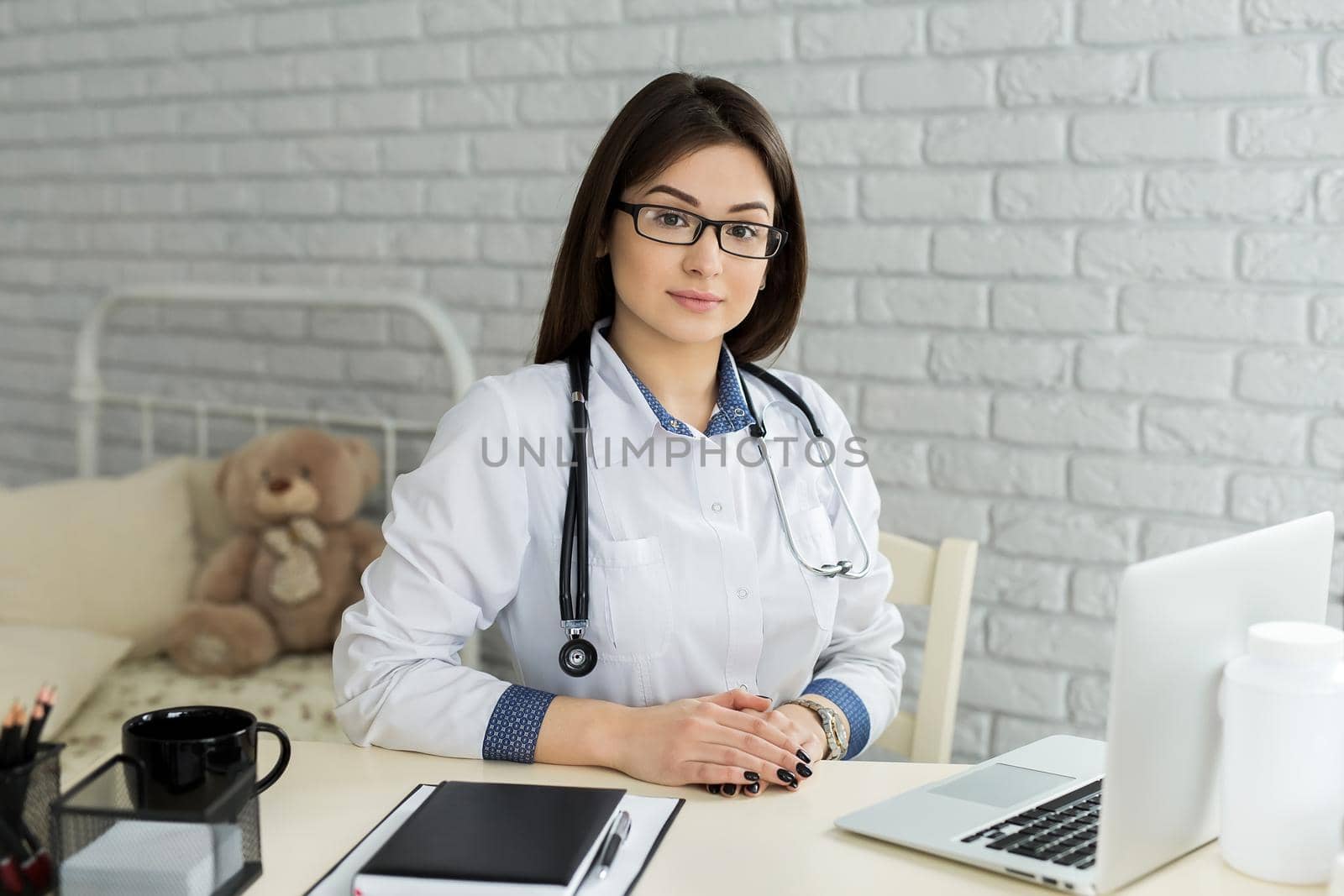 Portrait of cheerful happy female doctor sitting at her workplace. by StudioPeace