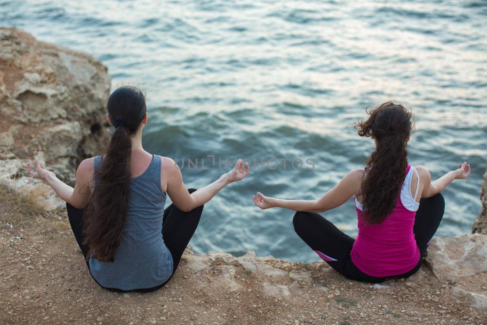 A couple of girls practicing yoga on the beach at sunset by StudioPeace