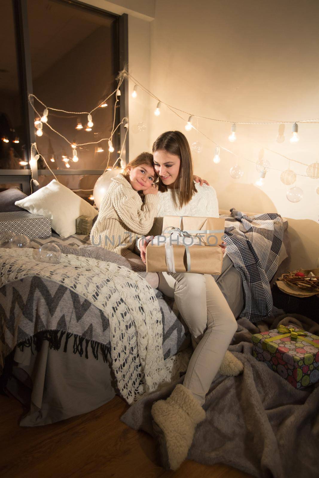Beautiful mother and daughter opening a magical Christmas gift in the cozy interior of the house. New year. by StudioPeace