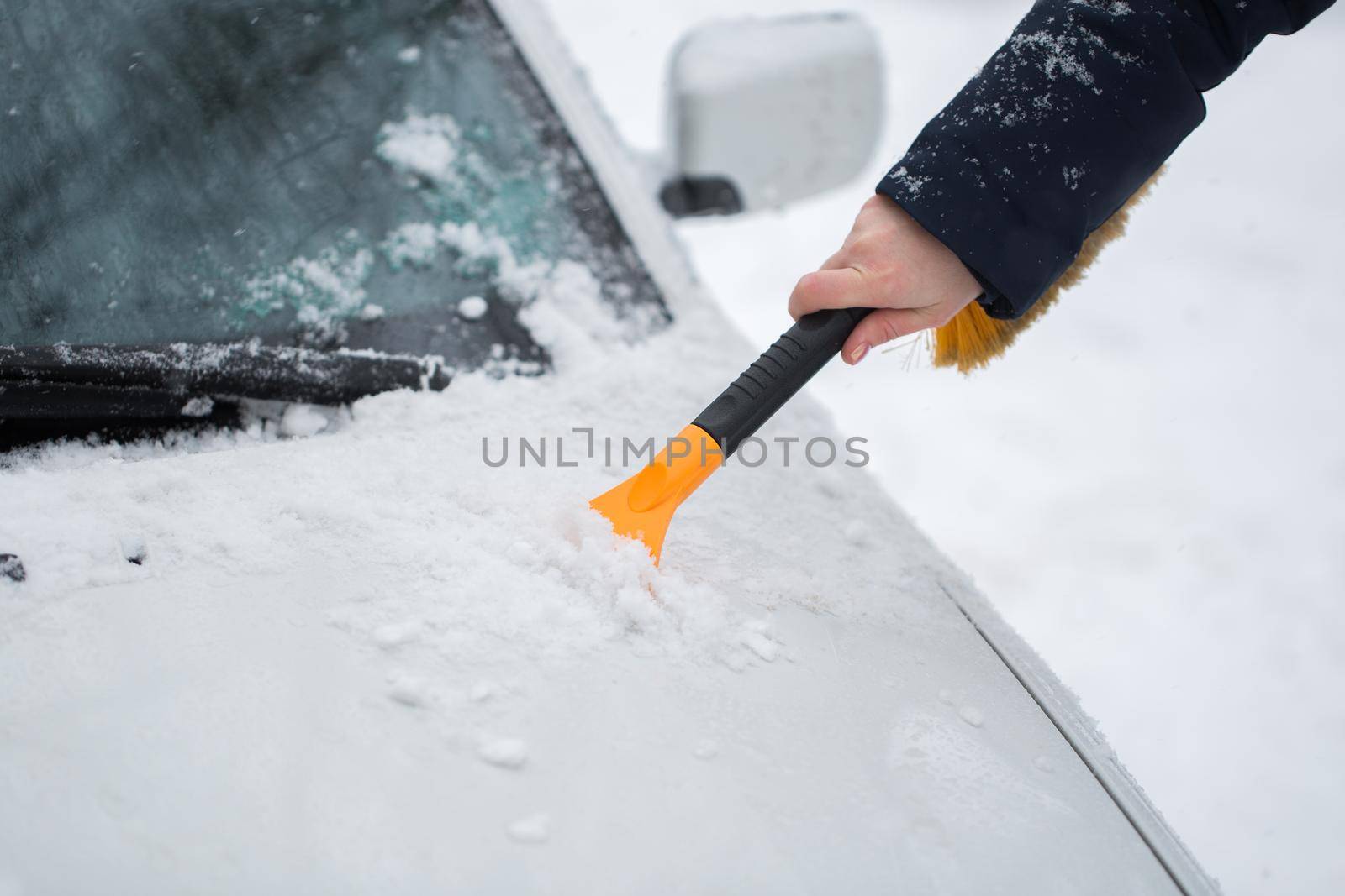 Woman cleaning snow from the car in the winter. by StudioPeace