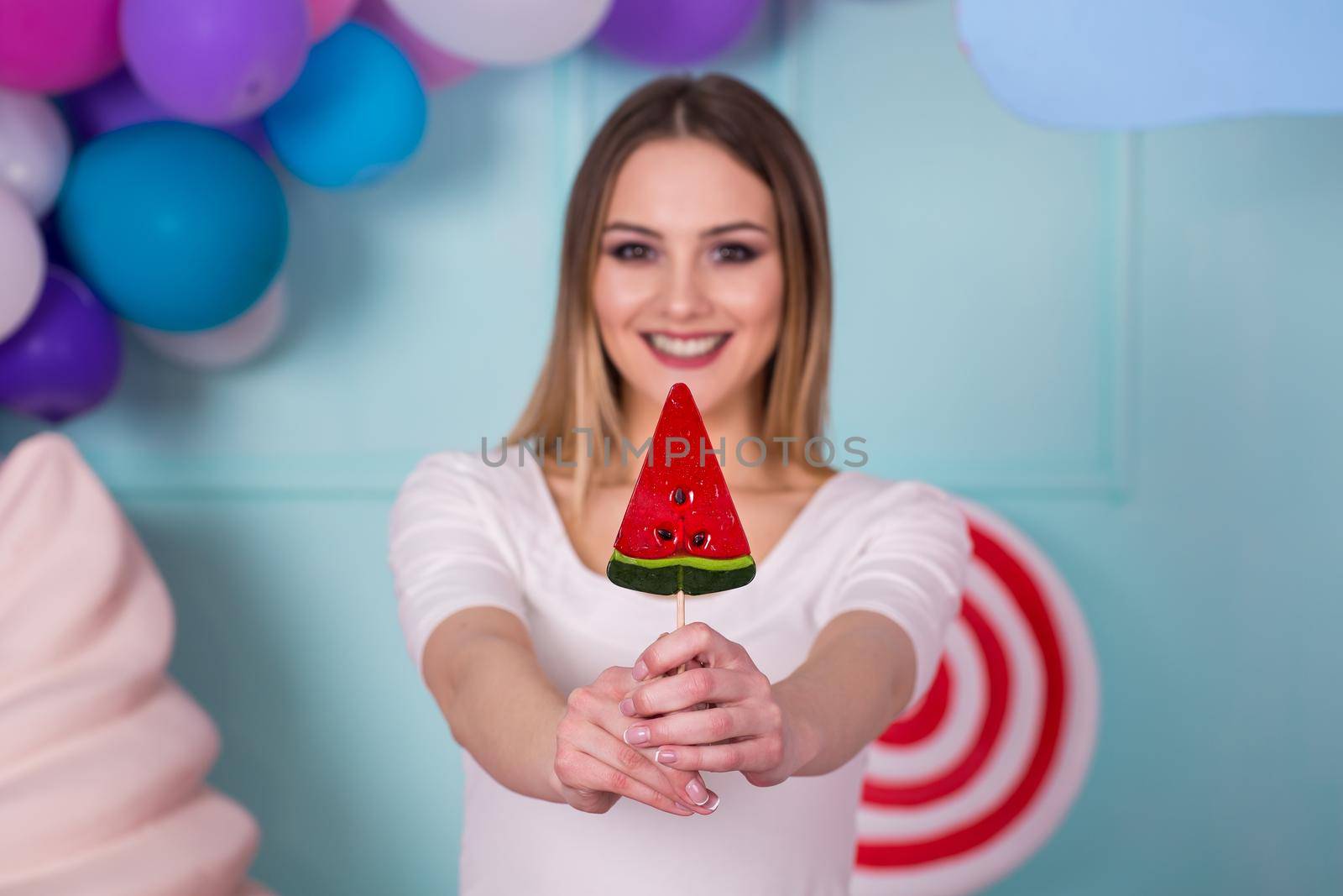 Portrait of amazing sweet-tooth woman in pink dress holding candies and posing on background decorated with huge ice cream. Lollipop watermelon. by StudioPeace