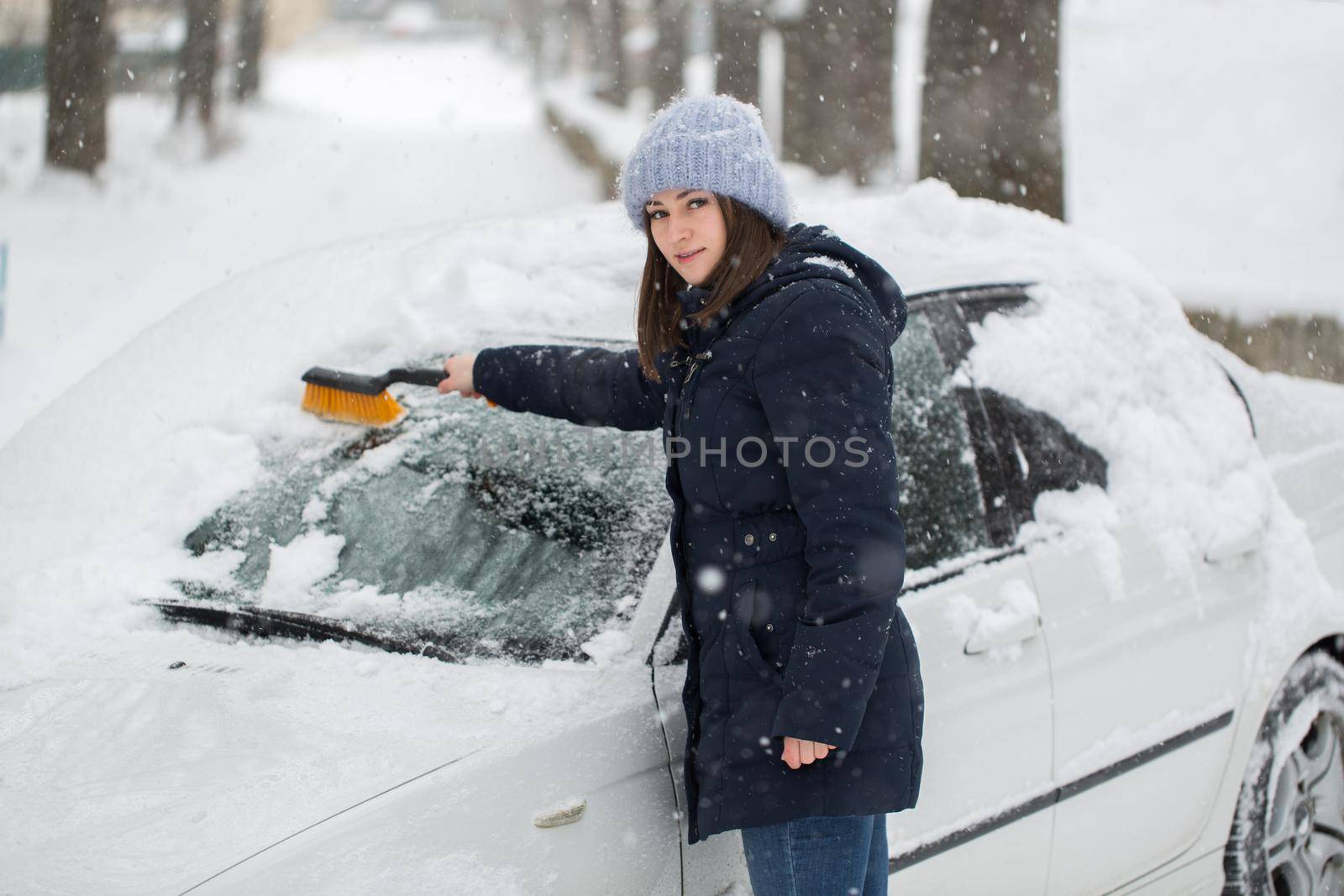 A woman removes snow from the windshield of a car. by StudioPeace