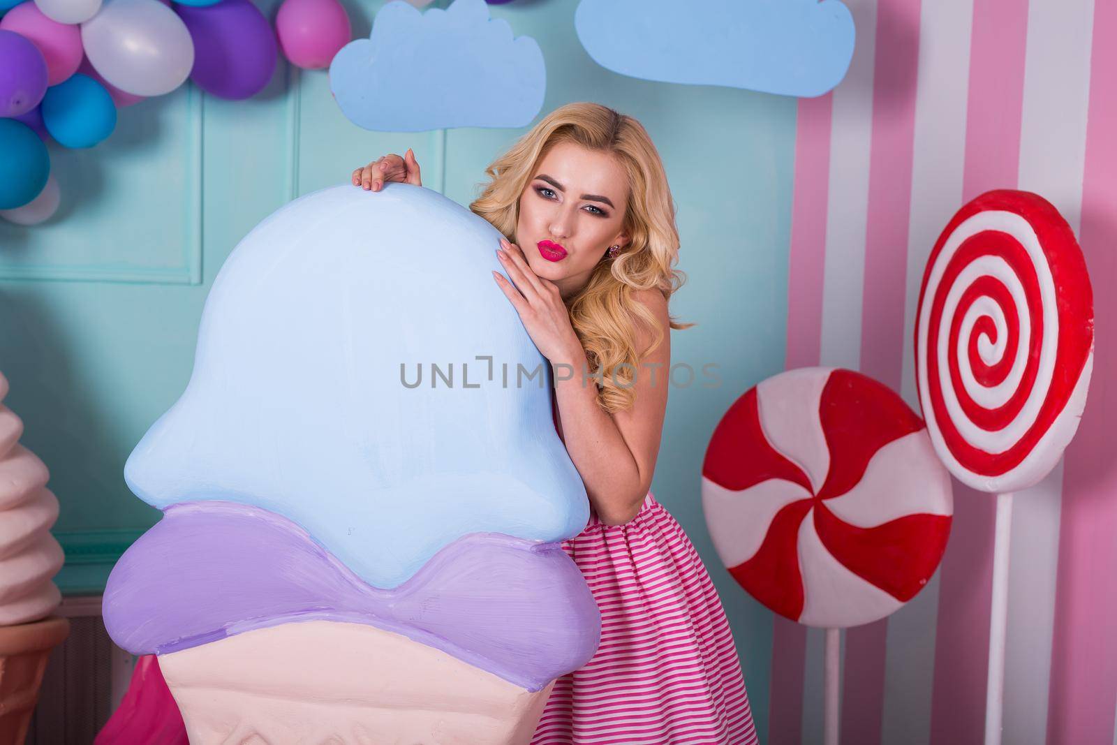 Portrait of young woman in pink dress holding big ice cream and posing on decorated background. Amazing sweet-tooth girl surrounded by toy sweets by StudioPeace