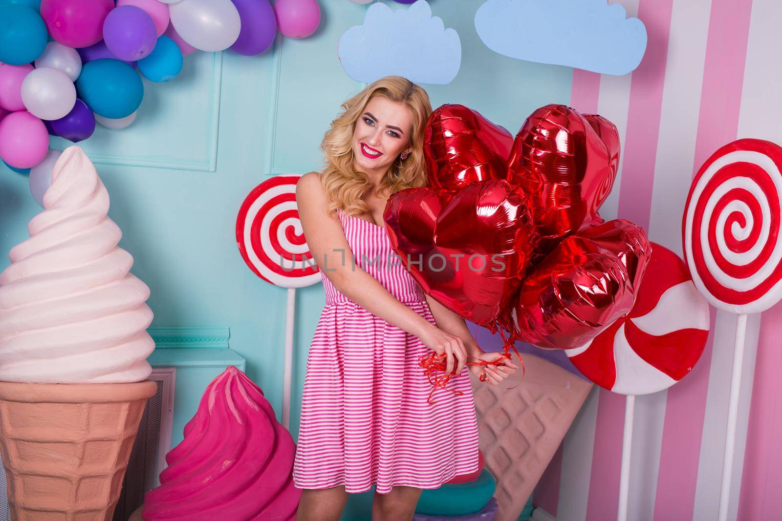 Fashion portrait of young woman in pink dress with an air balloons, candy on a colorful background.